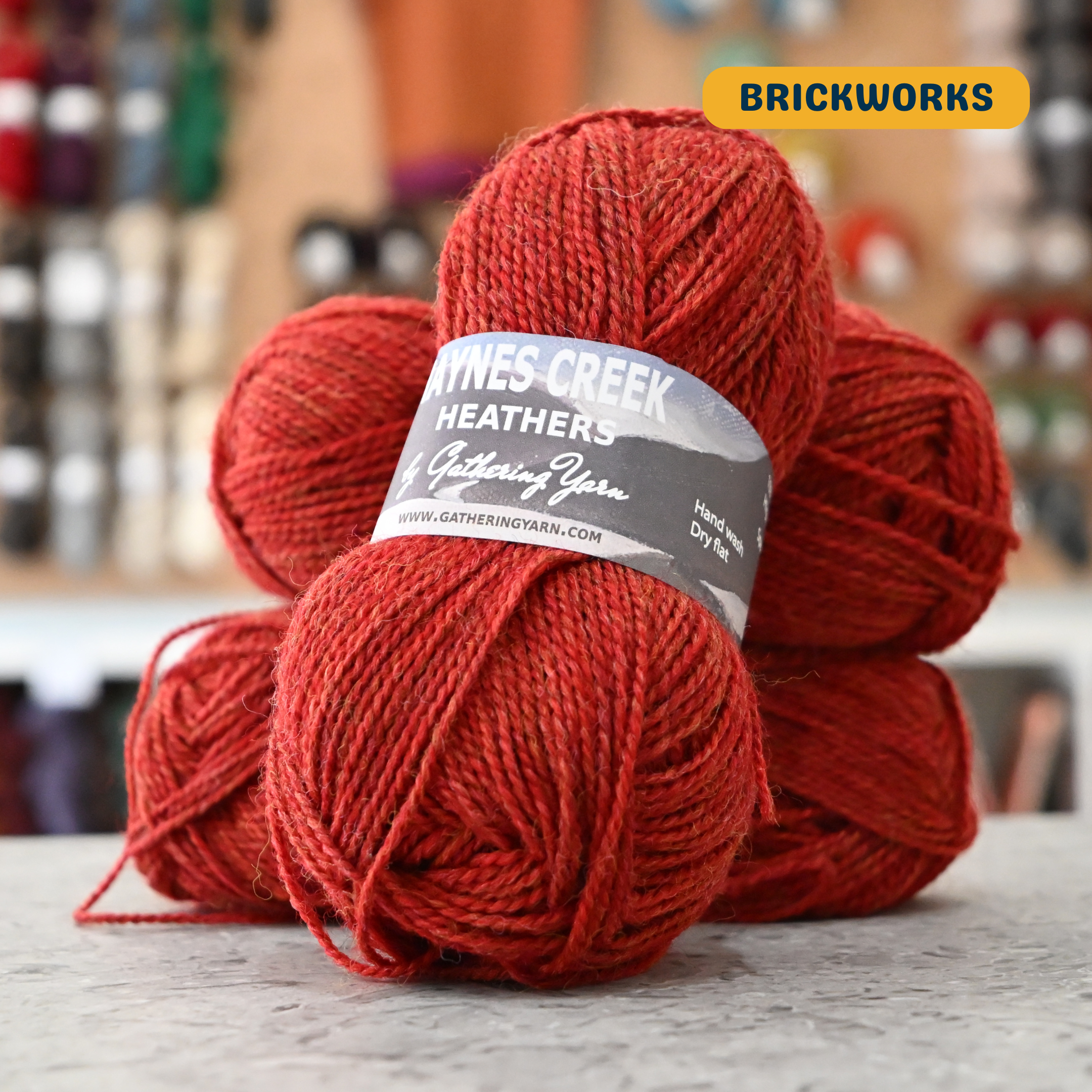 50g red (brickworks) Peruvian highland wool DK yarn, 'Haynes Creek Heathers by Gathering Yarn' label visible, craft shop background (blurred)