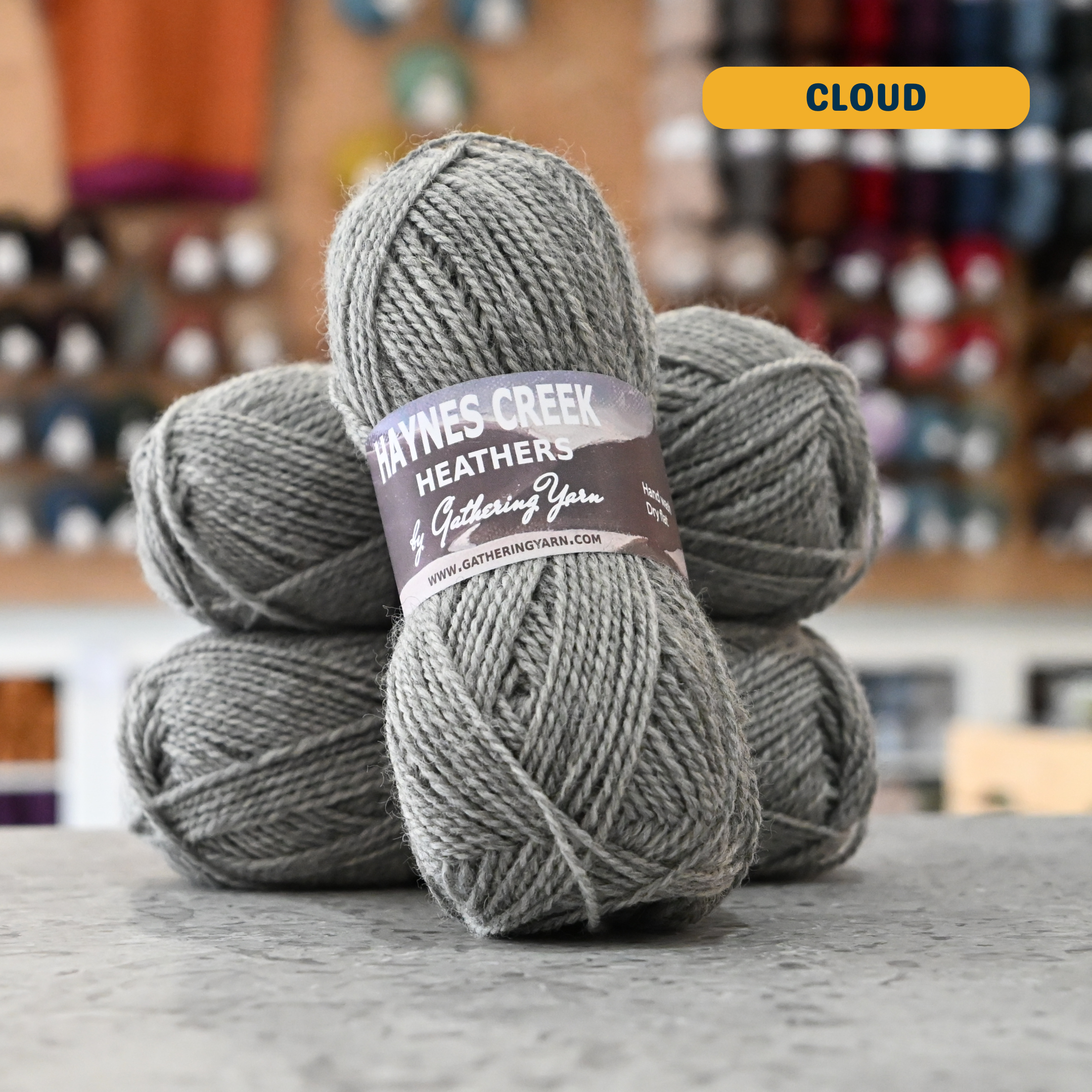 50g grey (cloud) Peruvian highland wool DK yarn, 'Haynes Creek Heathers by Gathering Yarn' label visible, craft shop background (blurred)