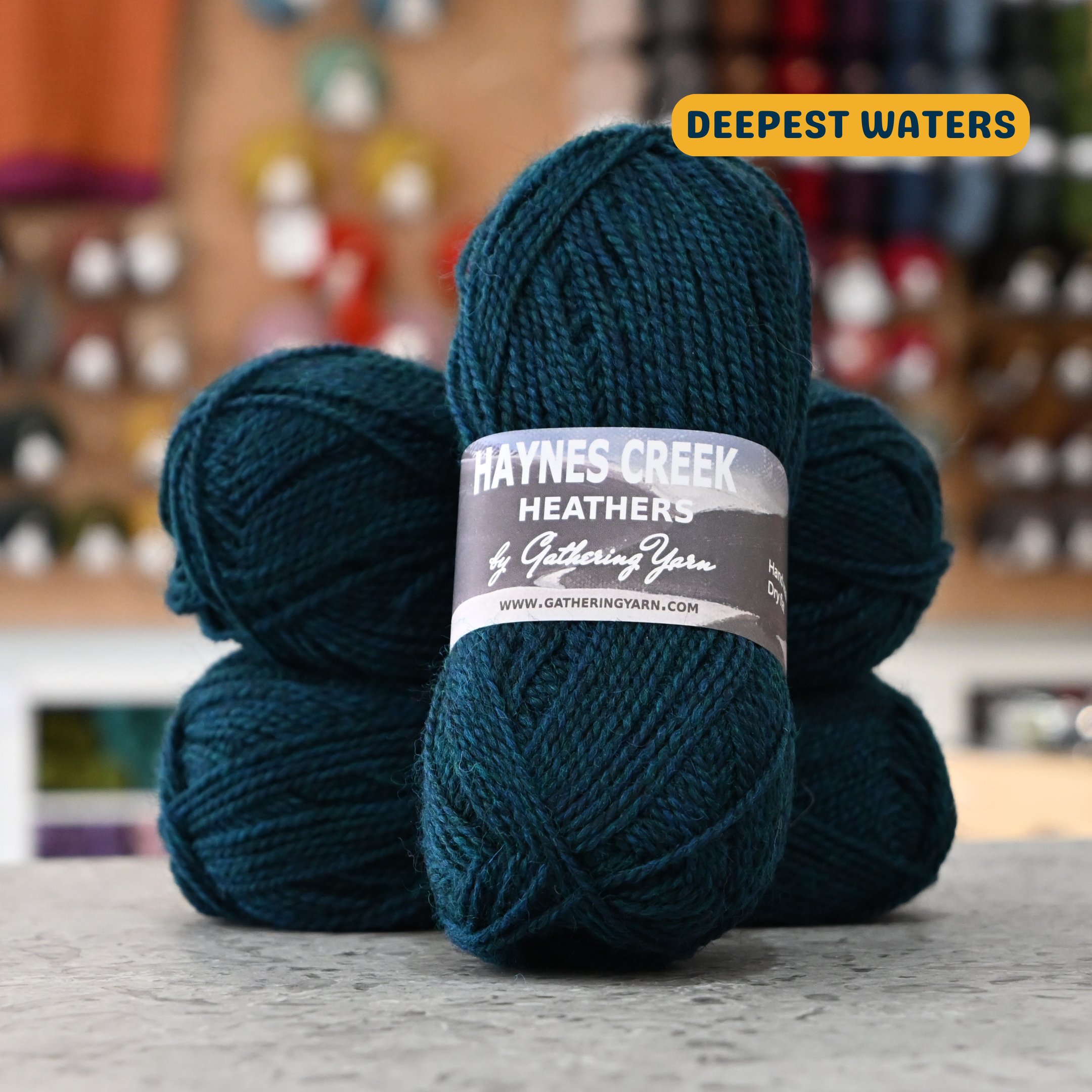 50g dark blue (deepest waters) Peruvian highland wool DK yarn, 'Haynes Creek Heathers by Gathering Yarn' label visible, craft shop background (blurred)