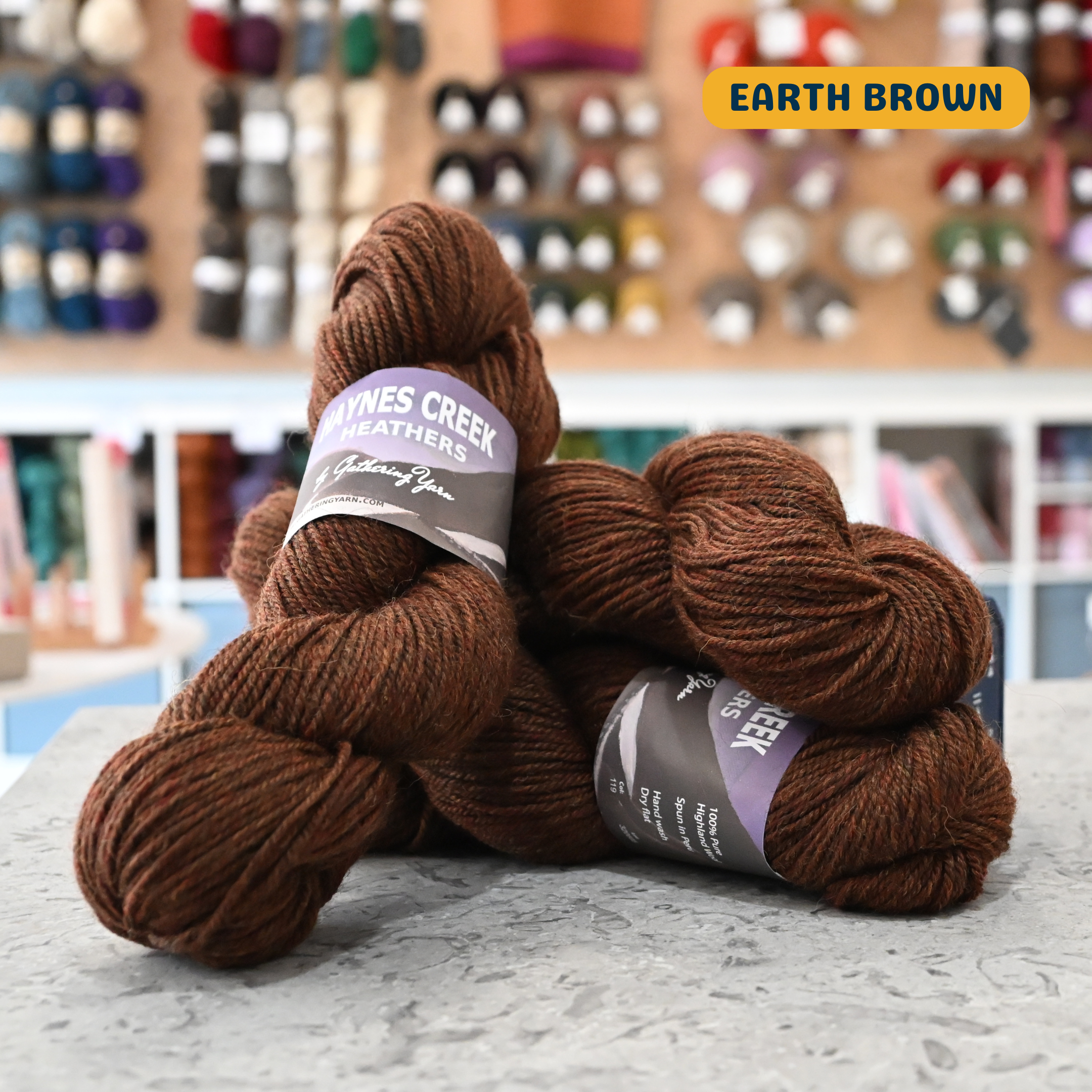 100g earth brown Peruvian highland wool worsted skeins, 'Haynes Creek Heathers by Gathering Yarn' label visible, craft shop background (blurred)