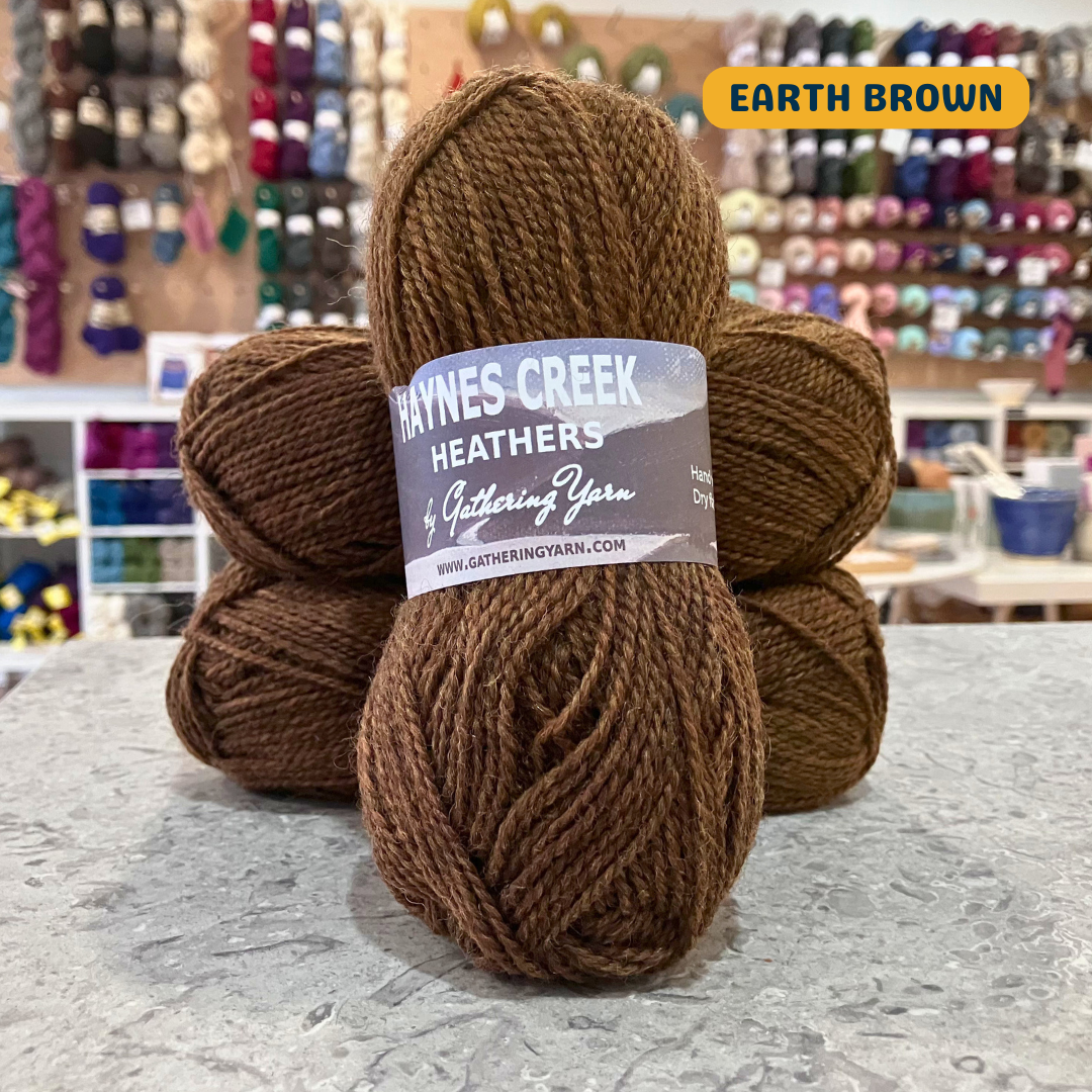 50g earth brown Peruvian highland wool DK yarn, 'Haynes Creek Heathers by Gathering Yarn' label visible, craft shop background (blurred)
