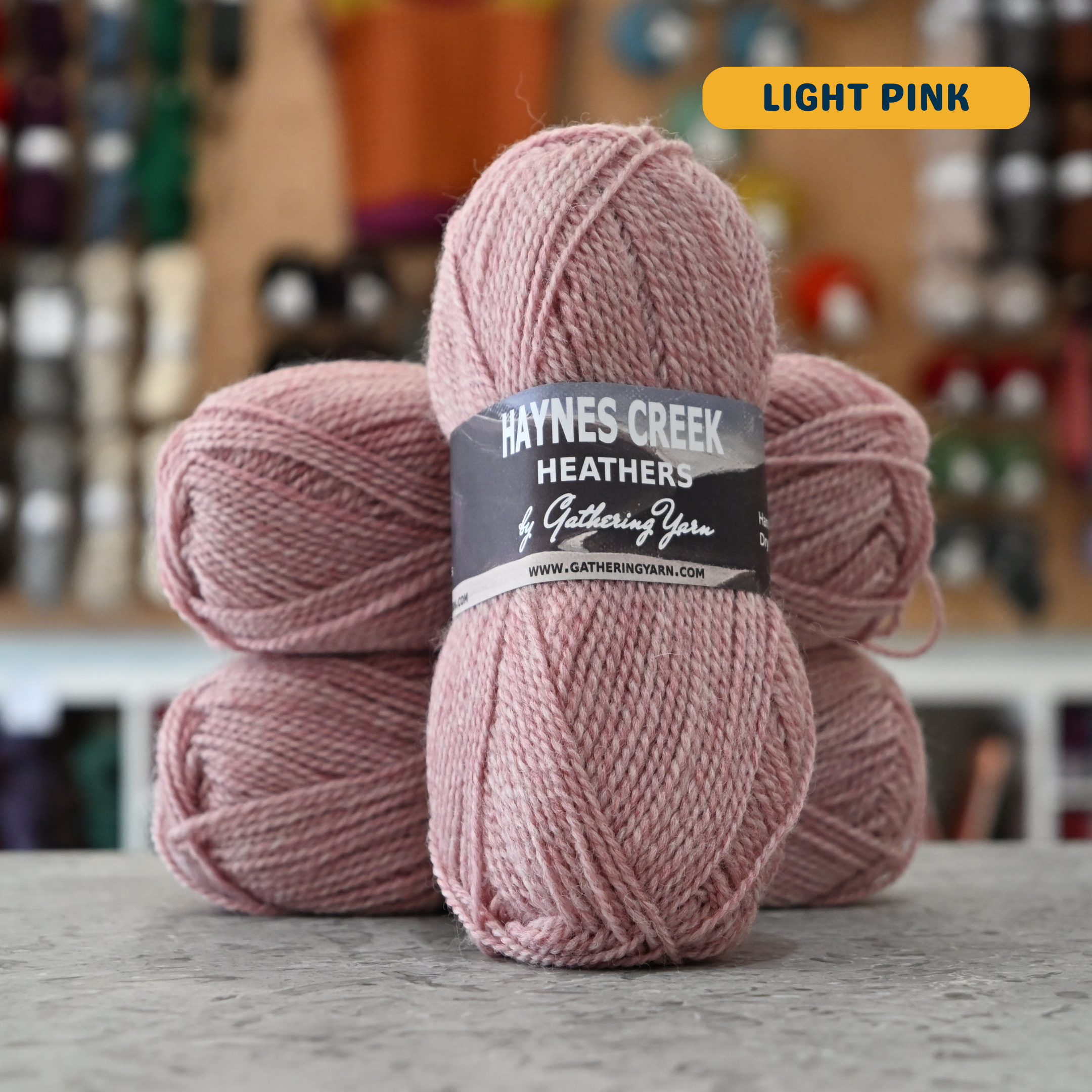 50g light pink Peruvian highland wool DK yarn, 'Haynes Creek Heathers by Gathering Yarn' label visible, craft shop background (blurred)
