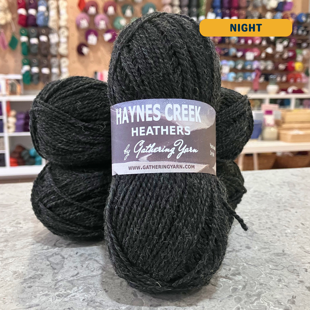 50g dark grey (night) Peruvian highland wool DK yarn, 'Haynes Creek Heathers by Gathering Yarn' label visible, craft shop background (blurred)