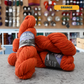 100g orange Peruvian highland wool worsted skeins, 'Haynes Creek Heathers by Gathering Yarn' label visible, craft shop background (blurred)