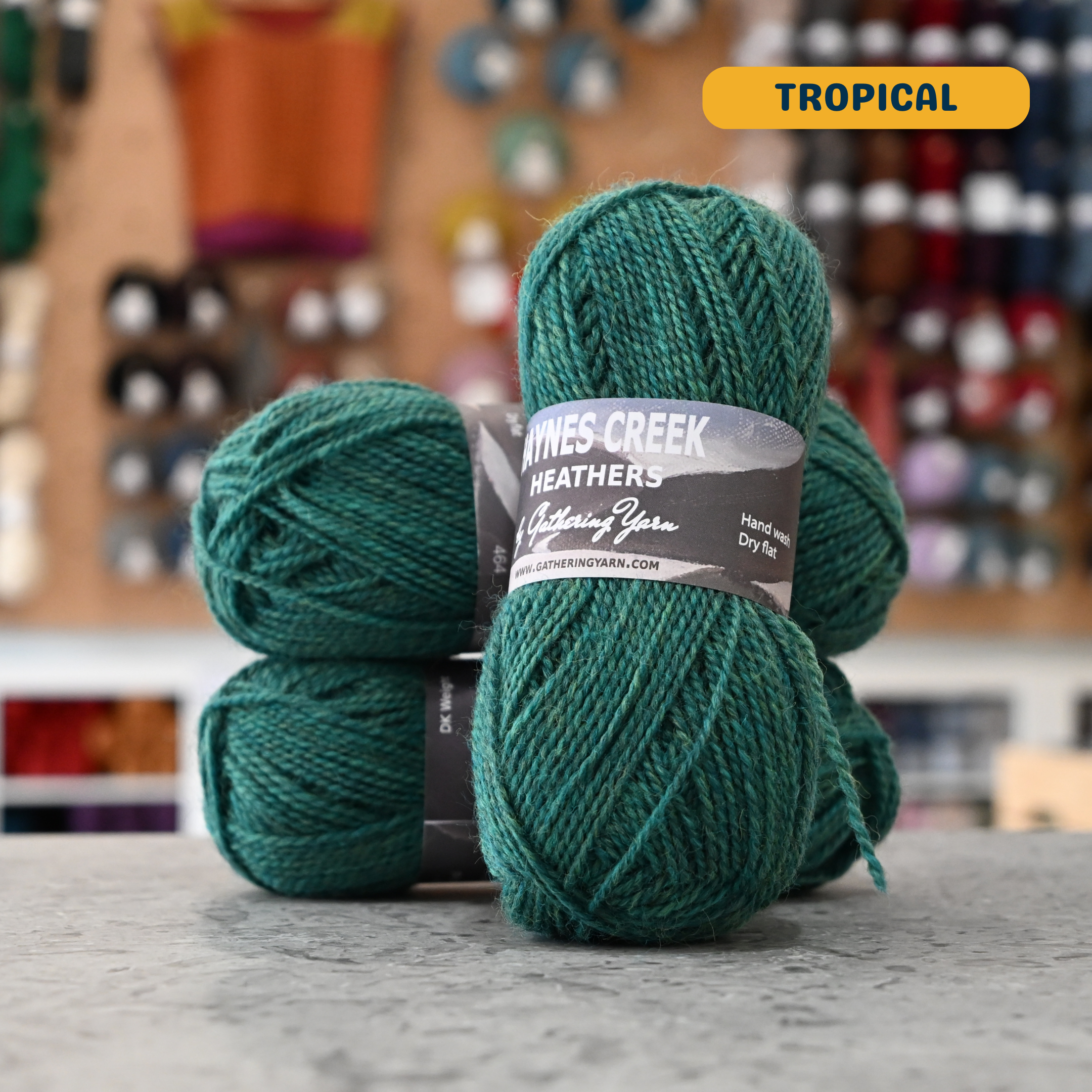 50g teal-green (tropical) Peruvian highland wool DK yarn, 'Haynes Creek Heathers by Gathering Yarn' label visible, craft shop background (blurred)