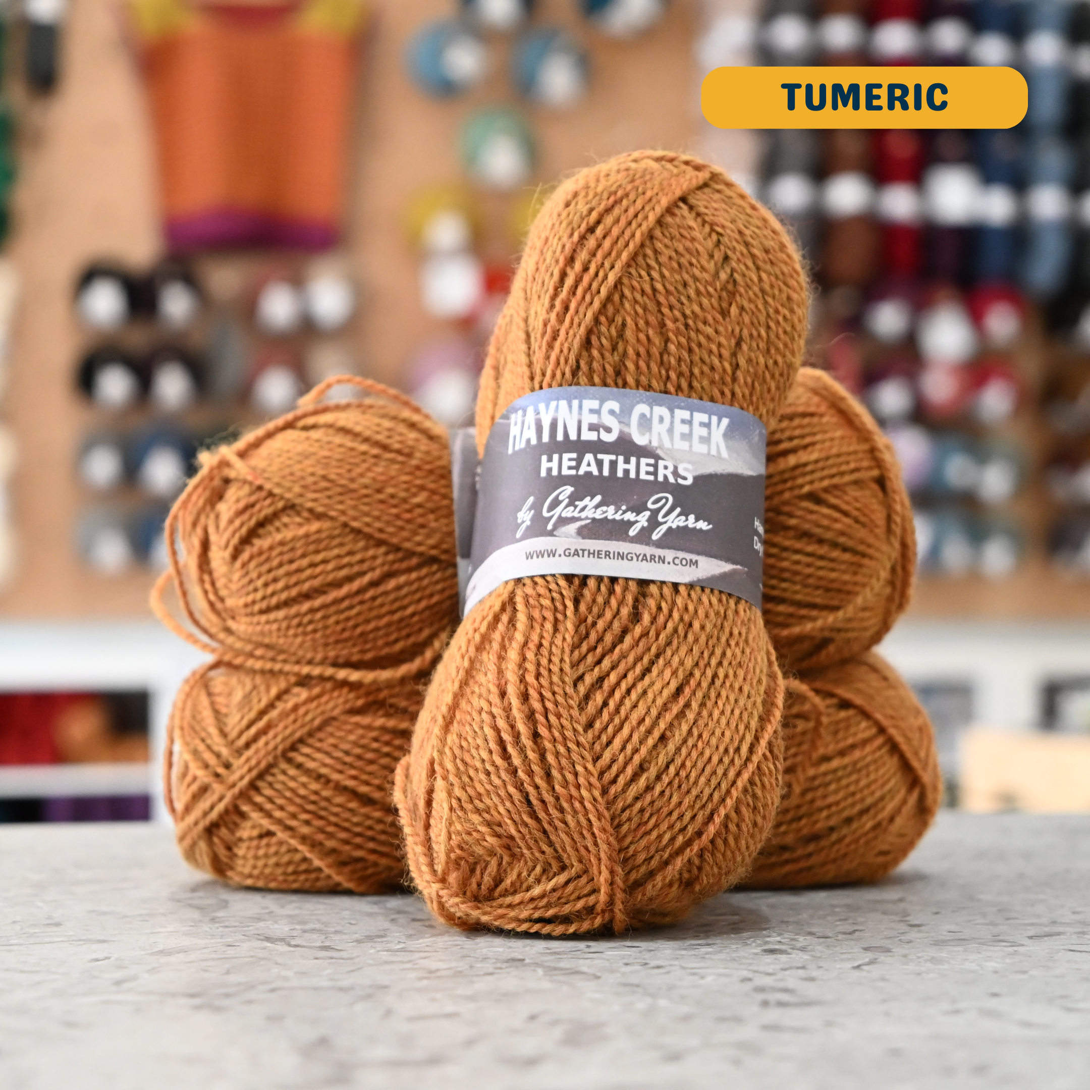 50g yellow-orange (tumeric) Peruvian highland wool DK yarn, 'Haynes Creek Heathers by Gathering Yarn' label visible, craft shop background (blurred)