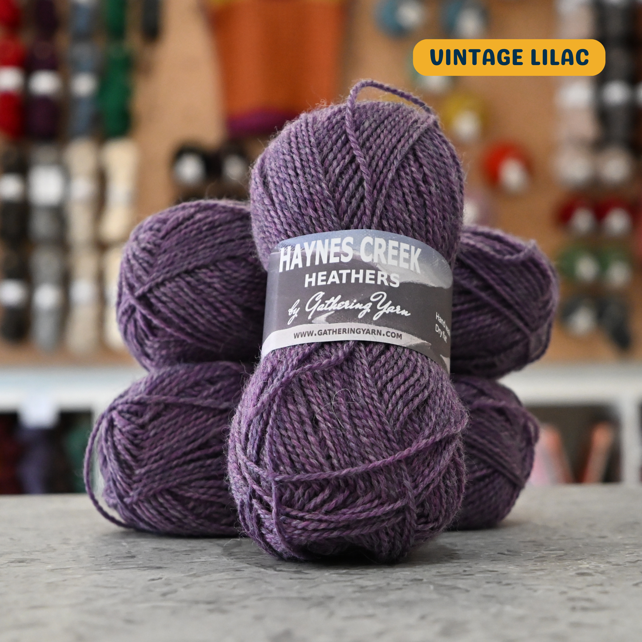 50g purple (vintage lilac) Peruvian highland wool DK yarn, 'Haynes Creek Heathers by Gathering Yarn' label visible, craft shop background (blurred)