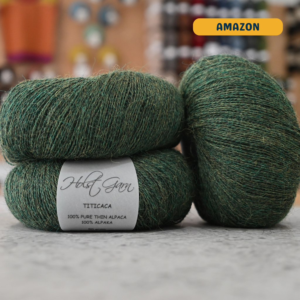 50g dark green (amazon) alpaca lace yarn, 'Holst Garn Titicaca 100% Pure Thin Alpaca' label visible, craft shop background (blurred)
