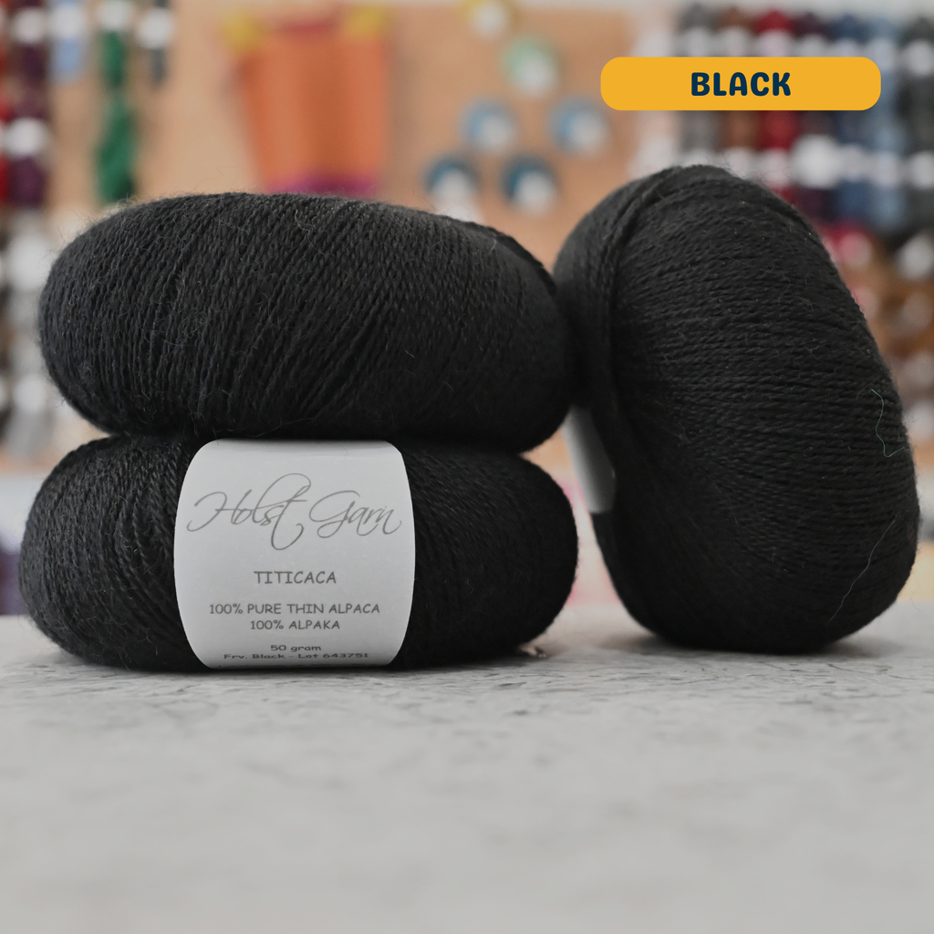 50g black alpaca lace yarn, 'Holst Garn Titicaca 100% Pure Thin Alpaca' label visible, craft shop background (blurred)