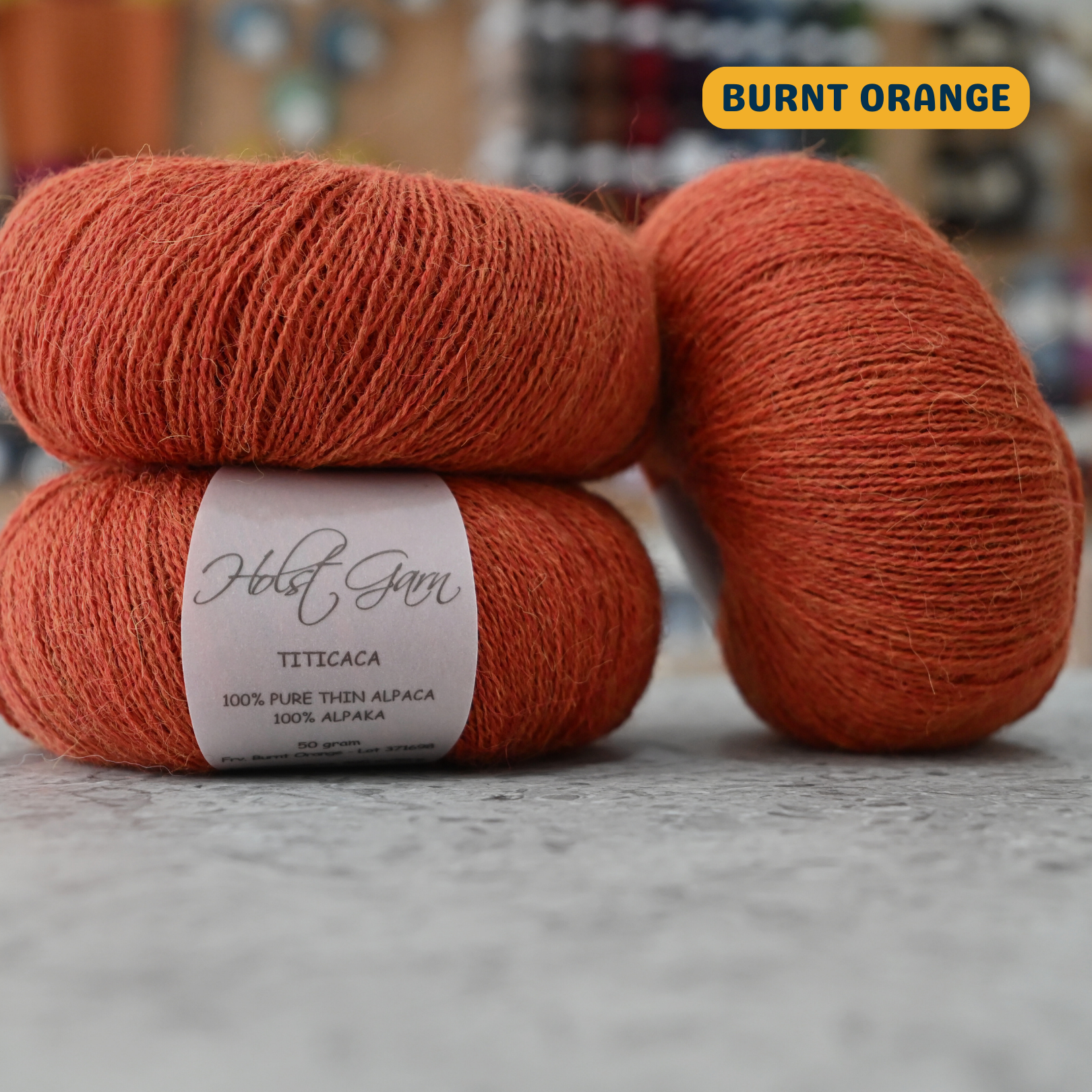 50g burnt orange alpaca lace yarn, 'Holst Garn Titicaca 100% Pure Thin Alpaca' label visible, craft shop background (blurred)