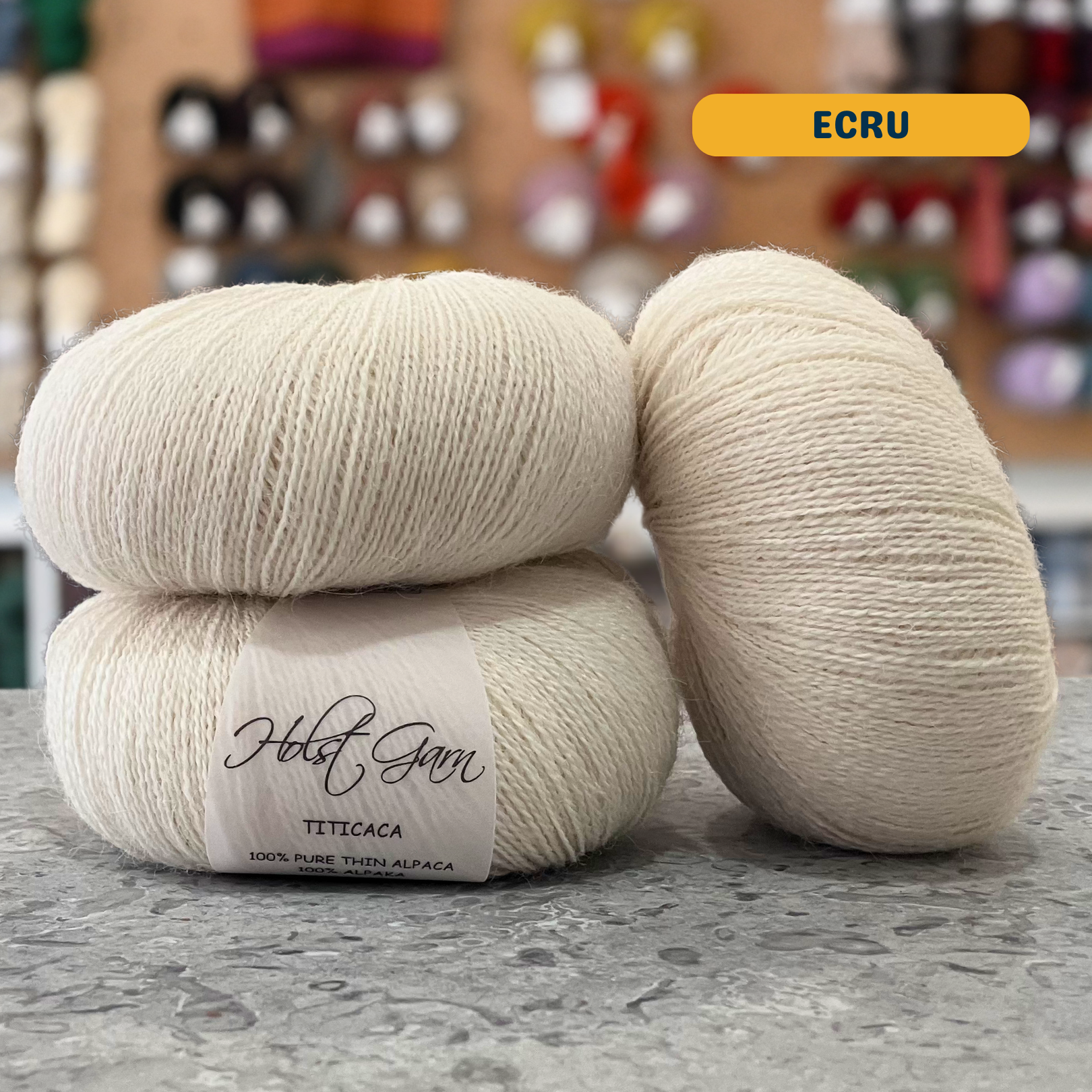 50g natural white (ecru) alpaca lace yarn, 'Holst Garn Titicaca 100% Pure Thin Alpaca' label visible, craft shop background (blurred)
