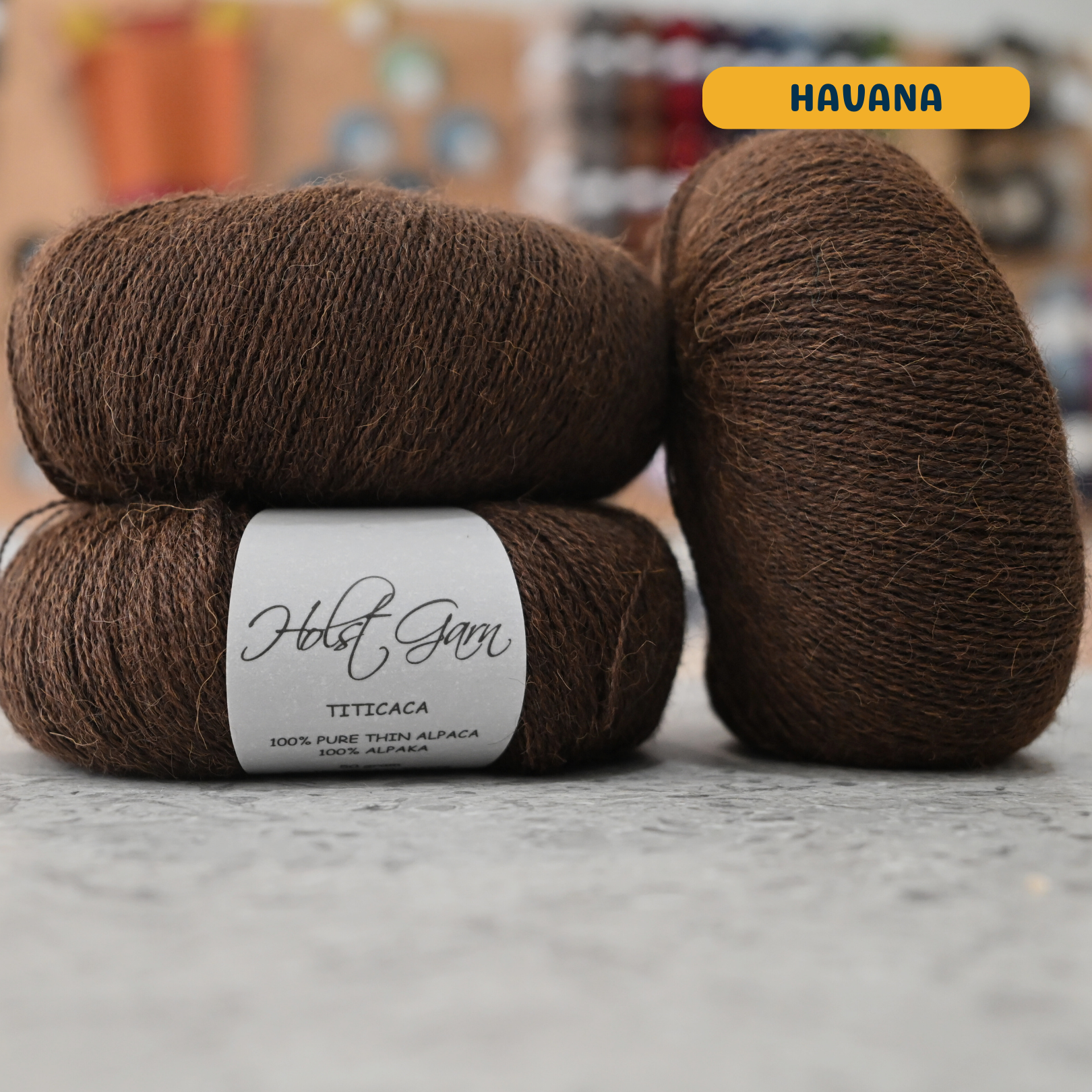 50g brown (havana) alpaca lace yarn, 'Holst Garn Titicaca 100% Pure Thin Alpaca' label visible, craft shop background (blurred)