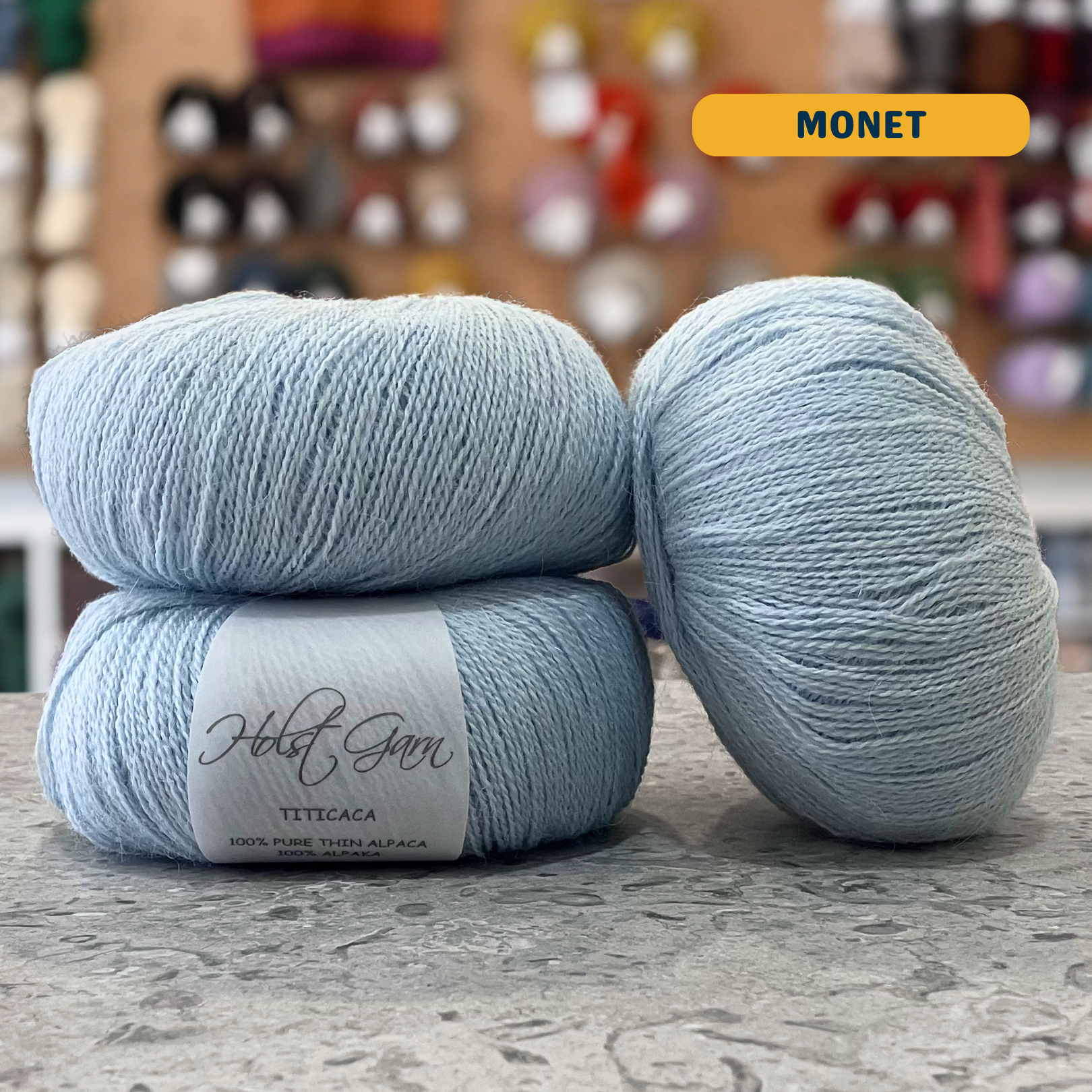 50g pale blue (monet) alpaca lace yarn, 'Holst Garn Titicaca 100% Pure Thin Alpaca' label visible, craft shop background (blurred)