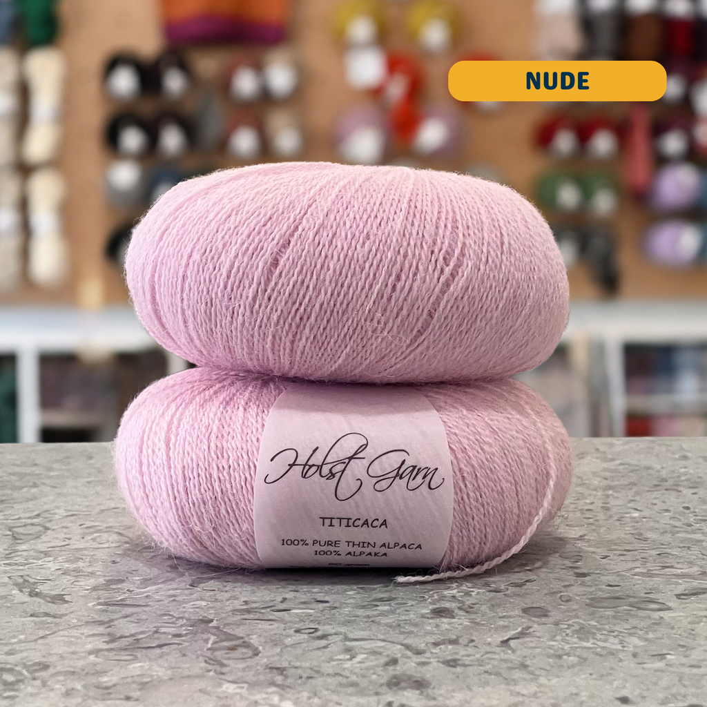50g pale pink (nude) alpaca lace yarn, 'Holst Garn Titicaca 100% Pure Thin Alpaca' label visible, craft shop background (blurred)
