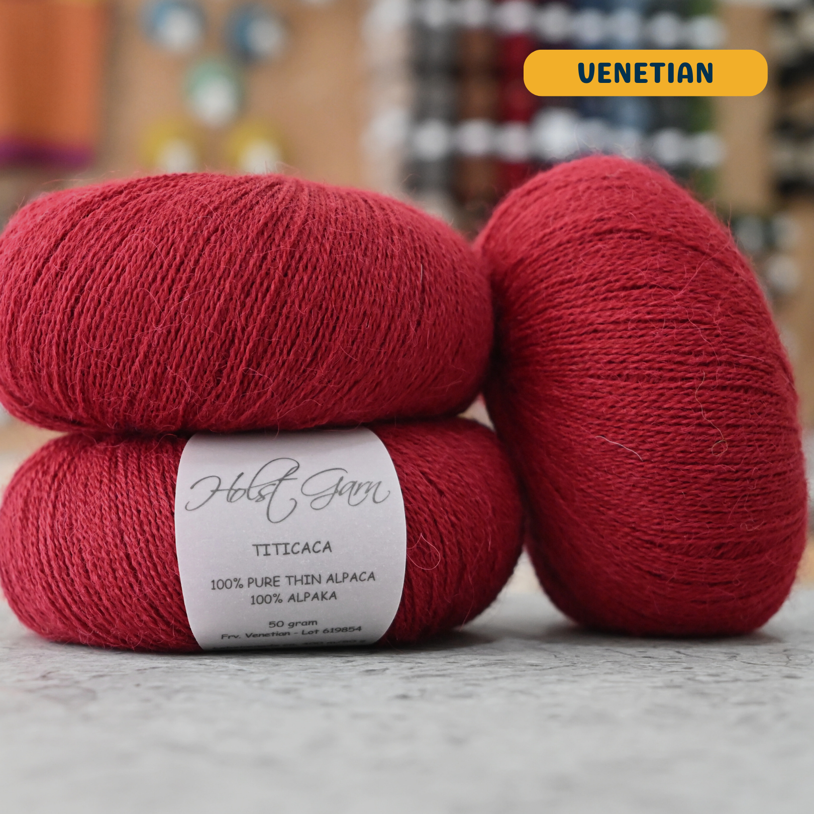50g red (venetian) alpaca lace yarn, 'Holst Garn Titicaca 100% Pure Thin Alpaca' label visible, craft shop background (blurred)