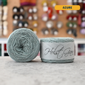 50g light azure lambswool‑merino‑cotton light fingering skein, 'Holst Garn' label visible, craft shop background (blurred)