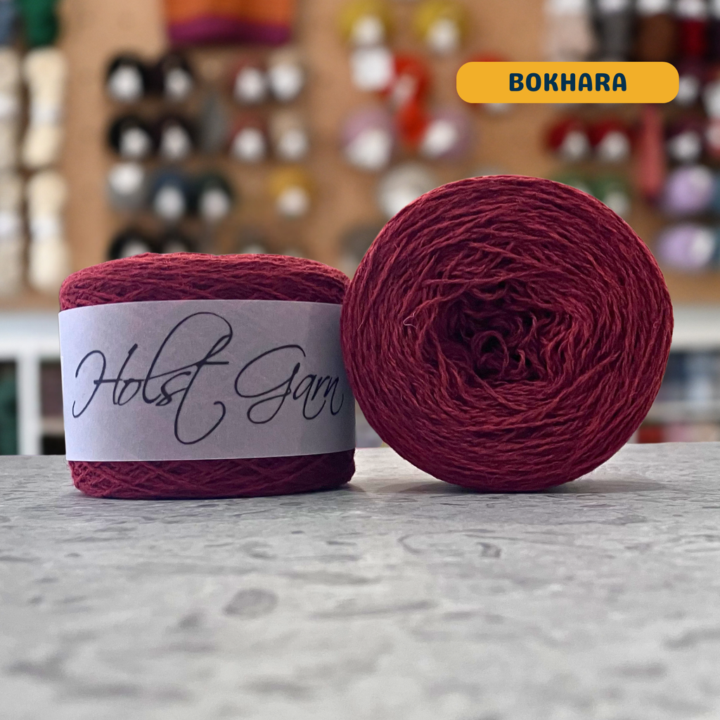 50g dark red (bokhara) merino & shetland wool light fingering yarn, 'Holst Garn' label visible, craft shop background (blurred)