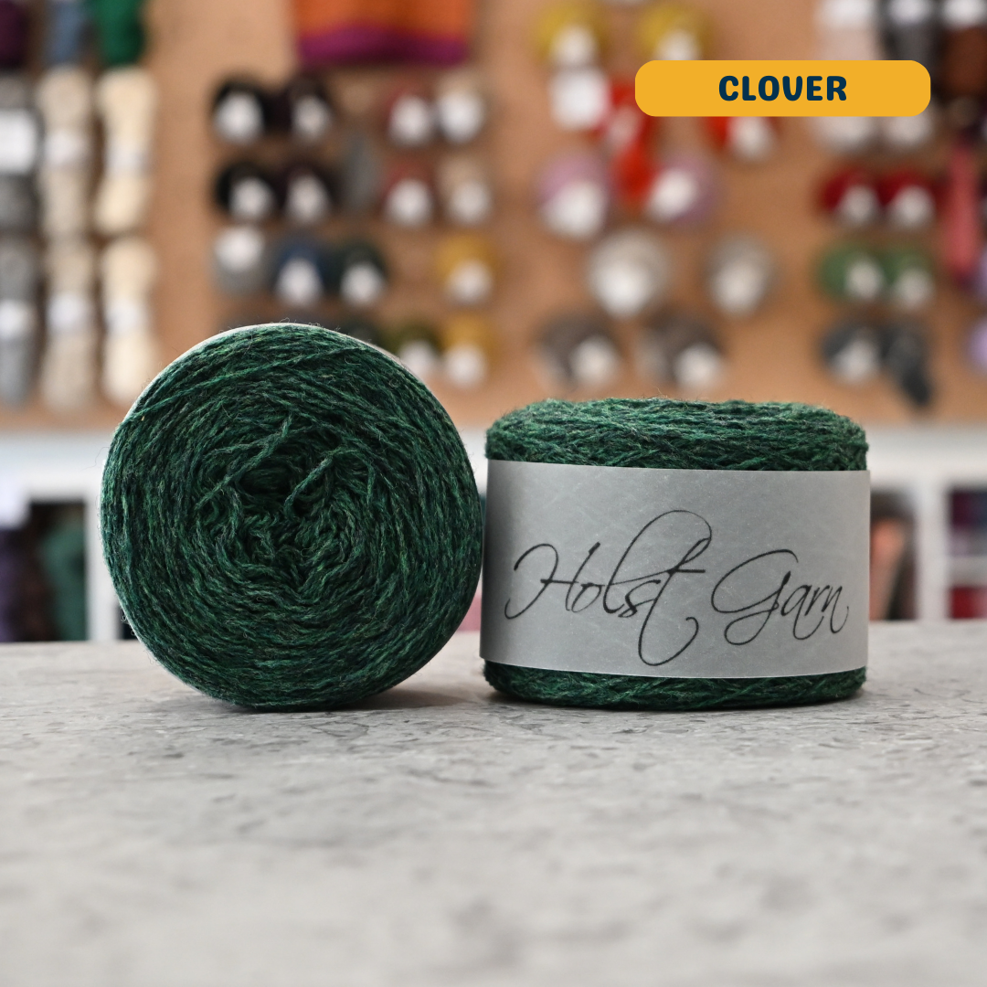 50g green (clover) merino & shetland wool light fingering yarn, 'Holst Garn' label visible, craft shop background (blurred)