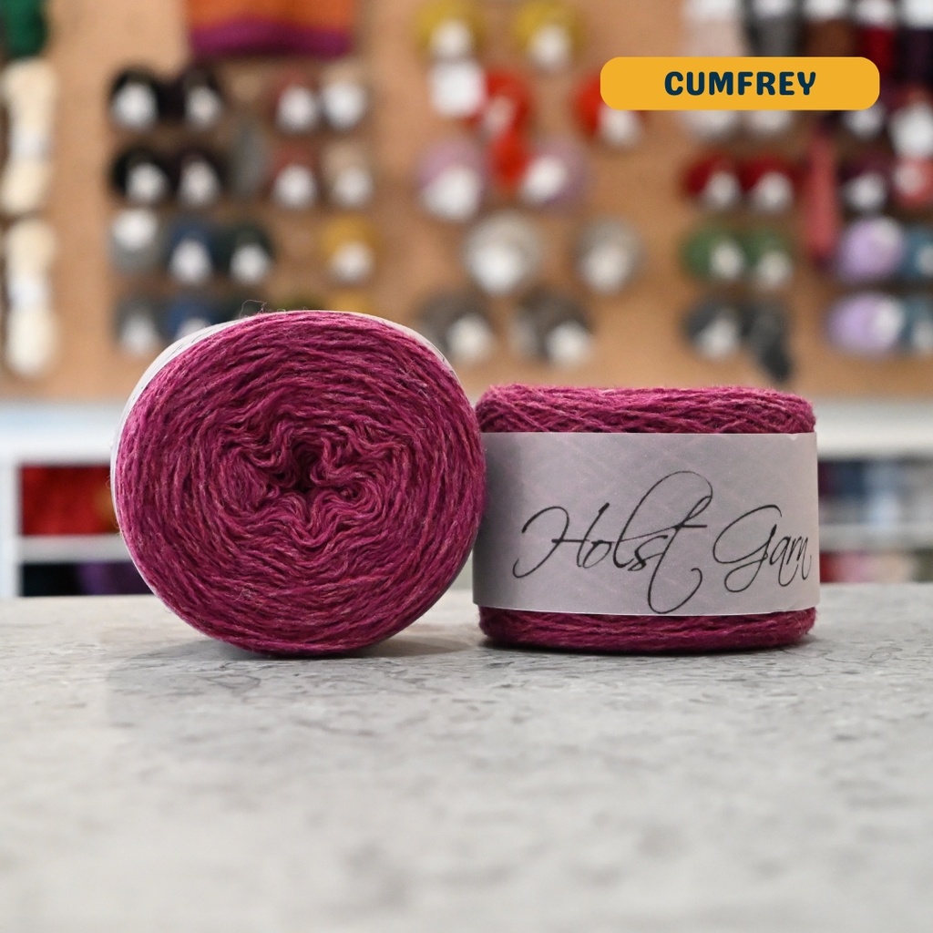 50g  dark pink (cumfrey) merino & shetland wool light fingering yarn, 'Holst Garn' label visible, craft shop background (blurred)