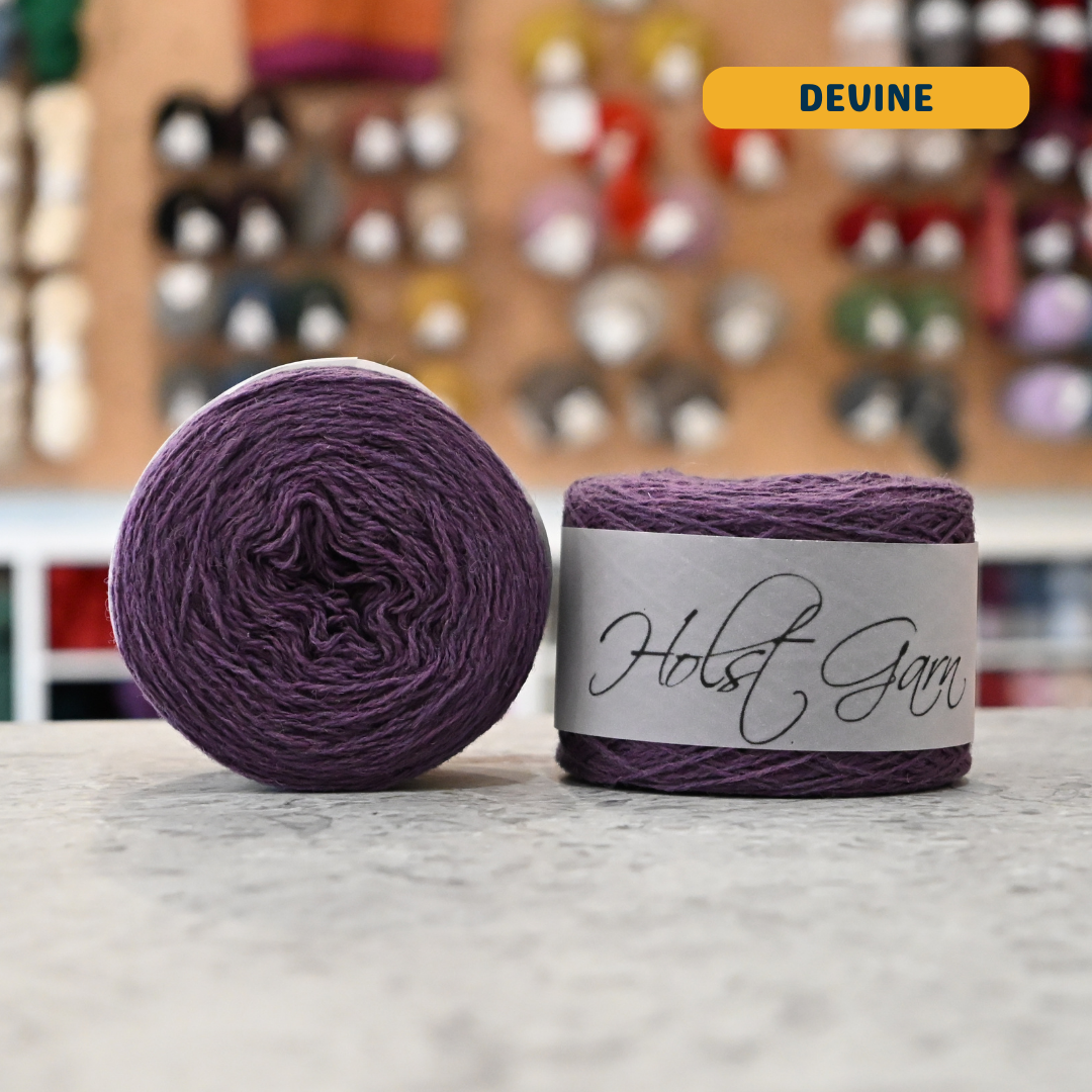 50g dark purple (devine) merino & shetland wool light fingering yarn, 'Holst Garn' label visible, craft shop background (blurred)