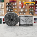 50g medium grey (flannel grey) merino & shetland wool light fingering yarn, 'Holst Garn' label visible, craft shop background (blurred)