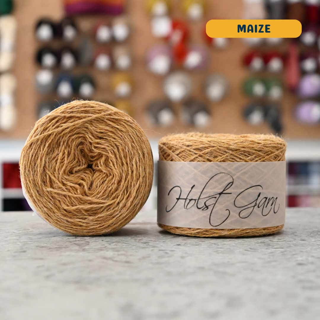 50g yellow (maize) merino & shetland wool light fingering yarn, 'Holst Garn' label visible, craft shop background (blurred)