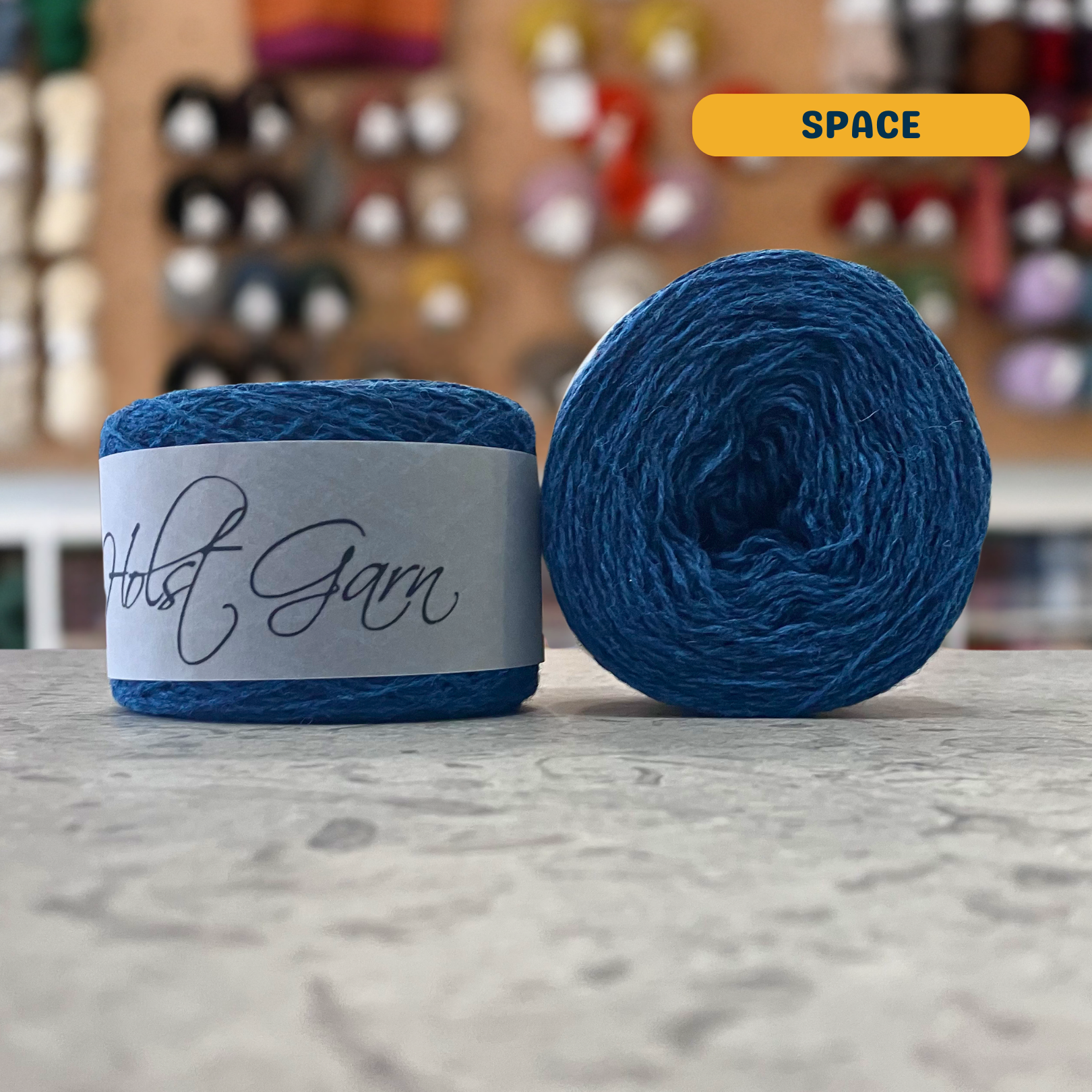 50g vibrant blue (space) merino & shetland wool light fingering yarn, 'Holst Garn' label visible, craft shop background (blurred)