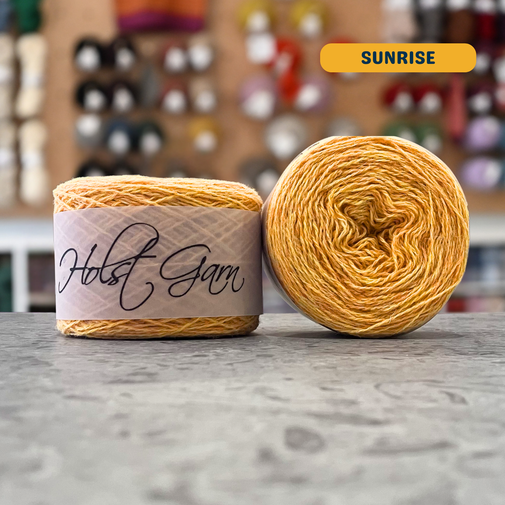 50g orange-yellow (sunrise) merino & shetland wool light fingering yarn, 'Holst Garn' label visible, craft shop background (blurred)