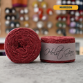 50g red (maroon) merino‑silk tweed light fingering skein, 'Holst Garn' label visible, craft shop background (blurred)