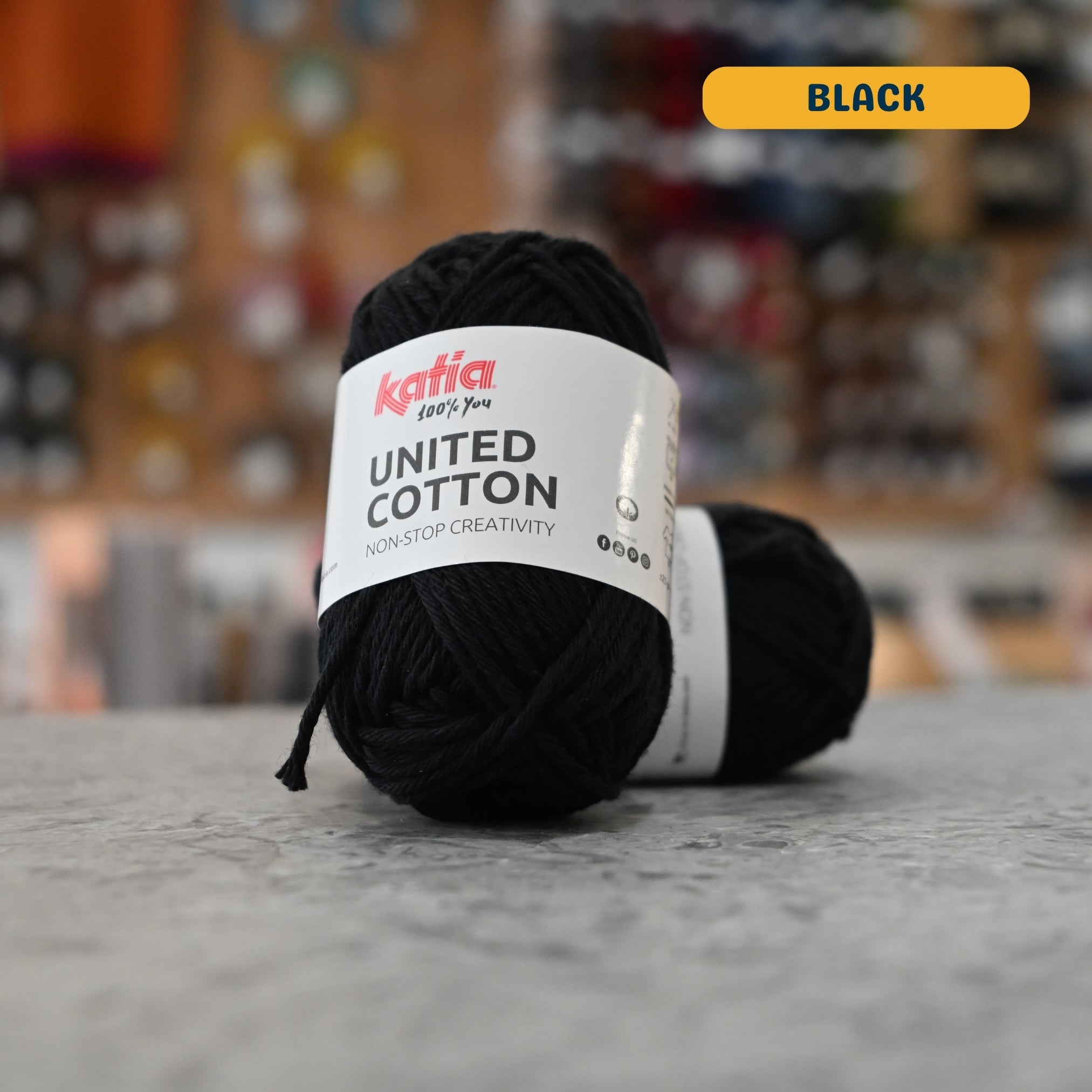 25g black cotton DK yarn, 'Katia United Cotton' label visible, craft shop background (blurred)