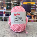 25g baby pink (rose) cotton DK yarn, 'Katia United Cotton' label visible, craft shop background (blurred)
