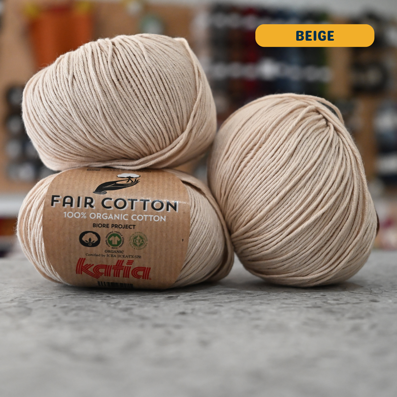 50g beige organic cotton sport yarn, 'Fair Cotton 100% Organic Cotton Katia' label visible, craft shop background (blurred)