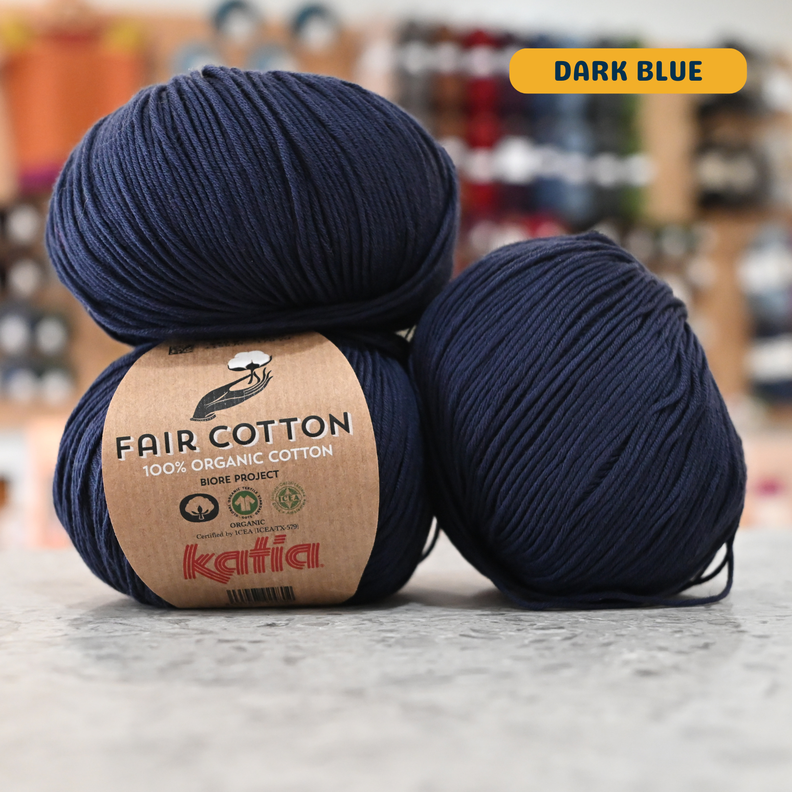 50g navy blue organic cotton sport yarn, 'Fair Cotton 100% Organic Cotton Katia' label visible, craft shop background (blurred)