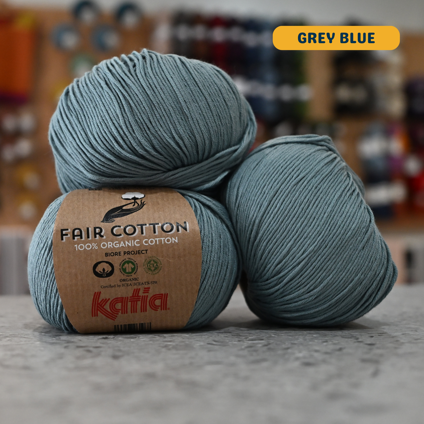 50g grey blue organic cotton sport yarn, 'Fair Cotton 100% Organic Cotton Katia' label visible, craft shop background (blurred)