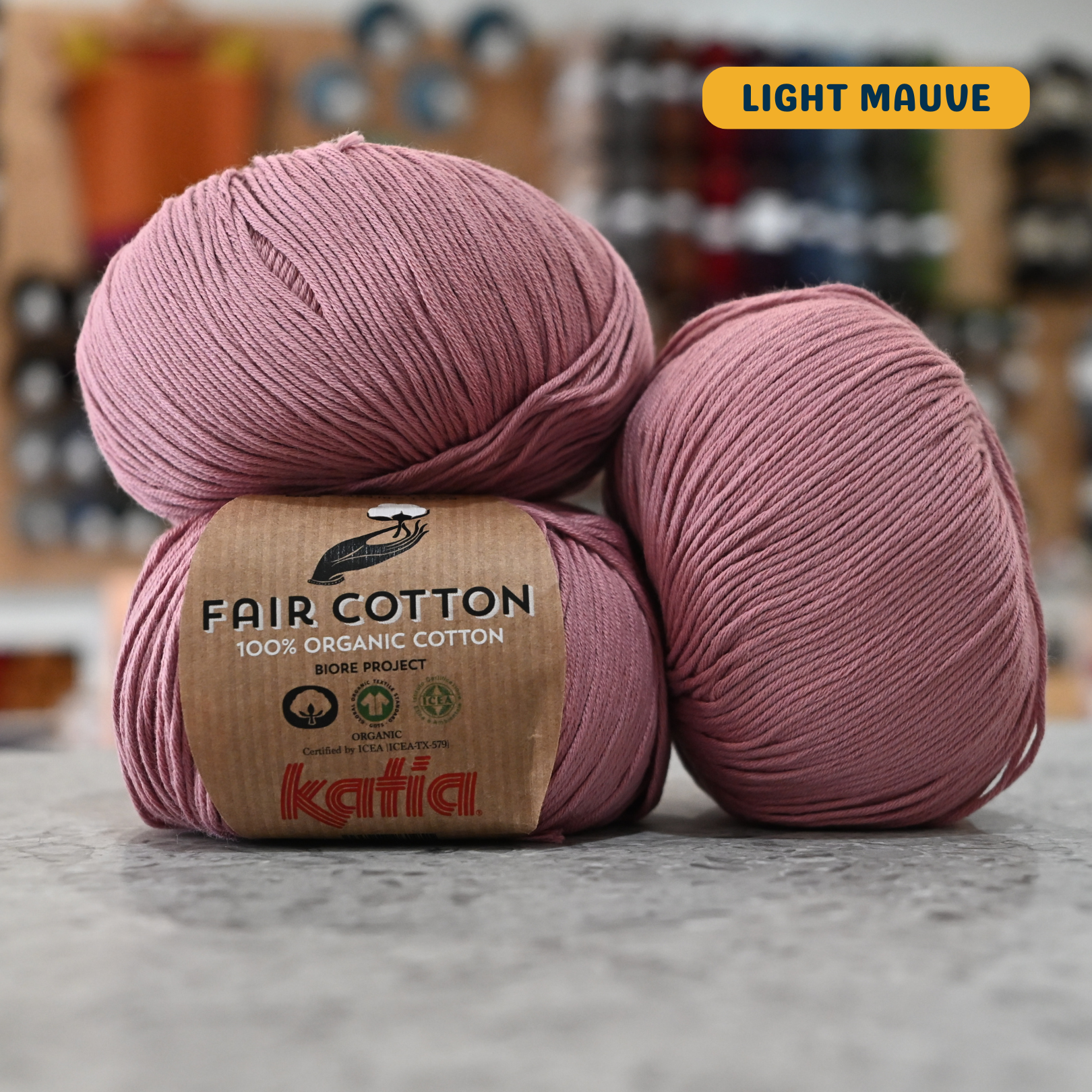 50g pink (light mauve) organic cotton sport yarn, 'Fair Cotton 100% Organic Cotton Katia' label visible, craft shop background (blurred)