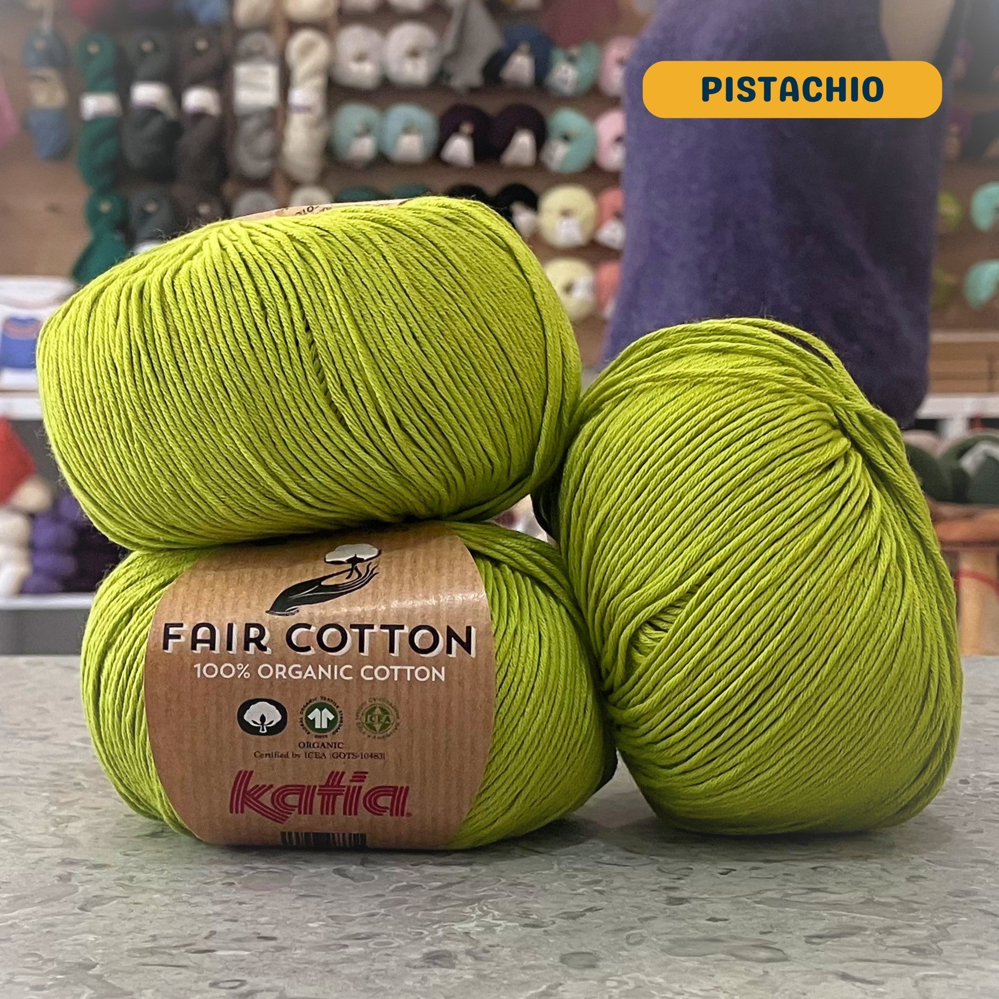 50g vibrant green (pistachio) organic cotton sport yarn, 'Fair Cotton 100% Organic Cotton Katia' label visible, craft shop background (blurred)