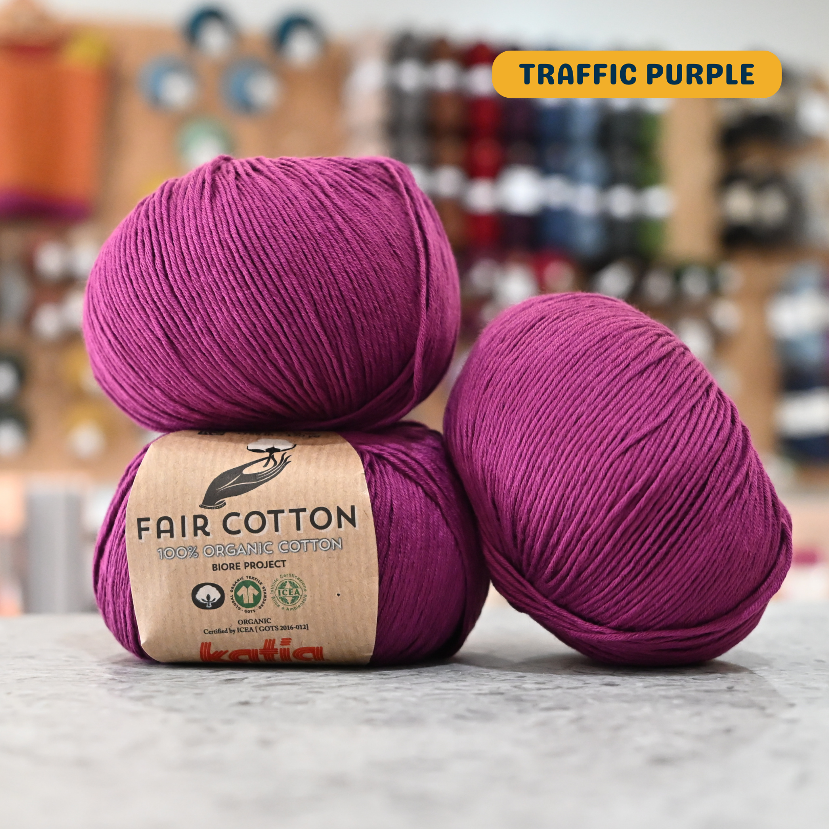 50g purple organic cotton sport yarn, 'Fair Cotton 100% Organic Cotton Katia' label visible, craft shop background (blurred)