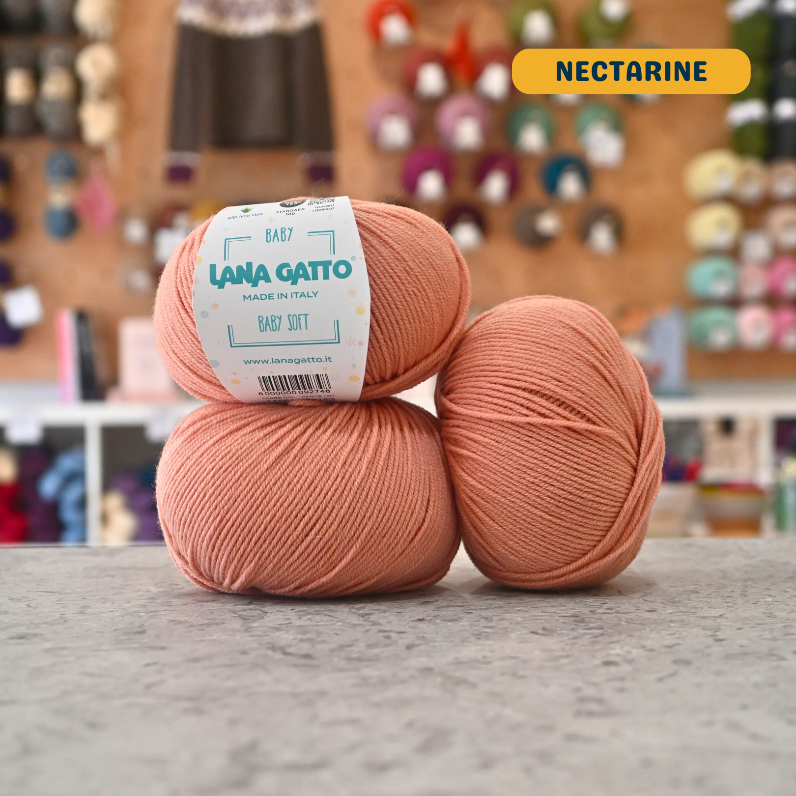 50g orange (nectarine) extrafine merino aloe vera sport yarn, 'Lana Gatto Baby Soft' label visible, craft shop background (blurred)