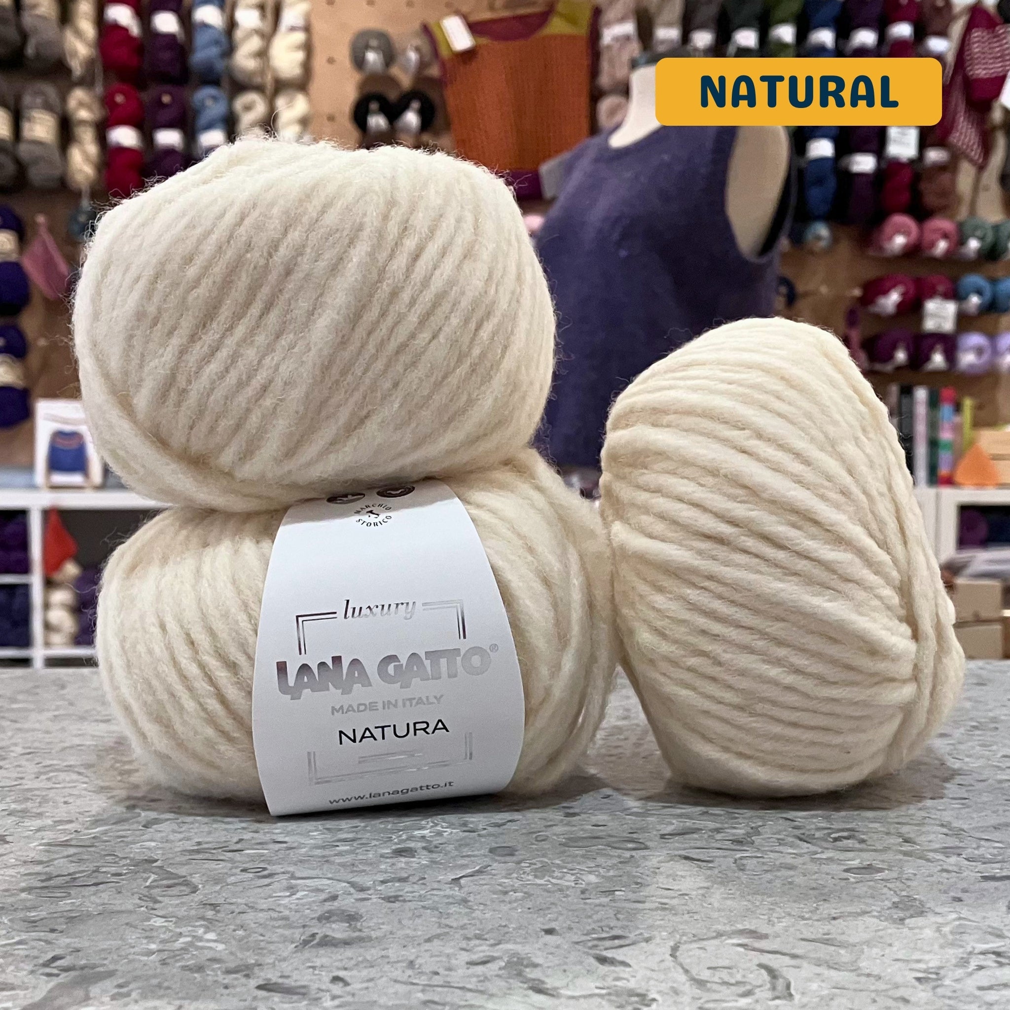 50g cream (natural) extrafine merino cotton baby alpaca bulky yarn, 'Luxury Lana Gatto Made In Italy Natura' label visible, craft shop background (blurred)