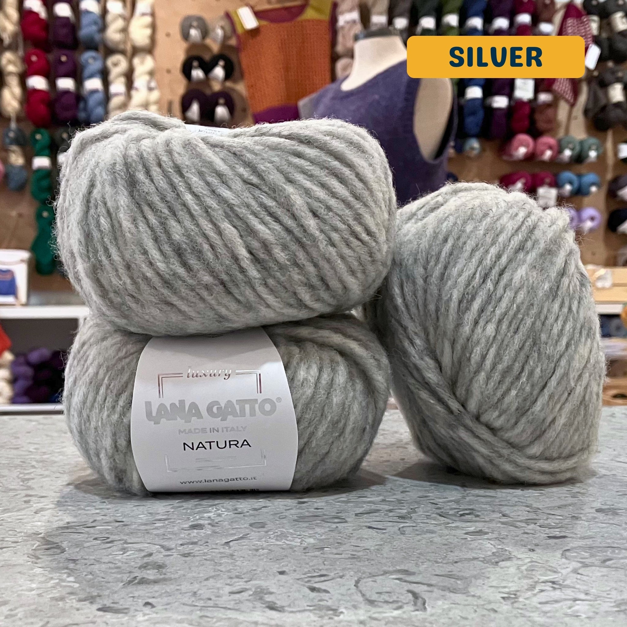 50g light grey (silver) extrafine merino cotton baby alpaca bulky yarn, 'Luxury Lana Gatto Made In Italy Natura' label visible, craft shop background (blurred)