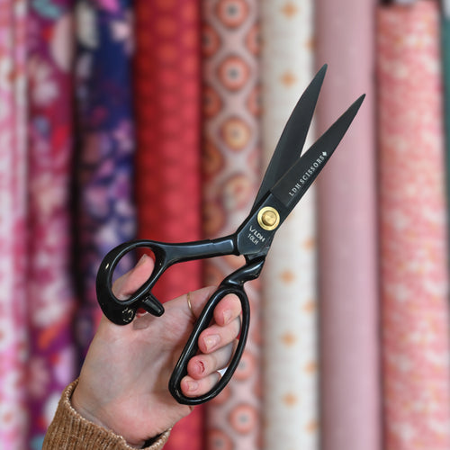 LDH Scissors 10 inch True Left-Handed Midnight Edition Fabric Shears in black carbon steel. Fabric bolts background (blurred).