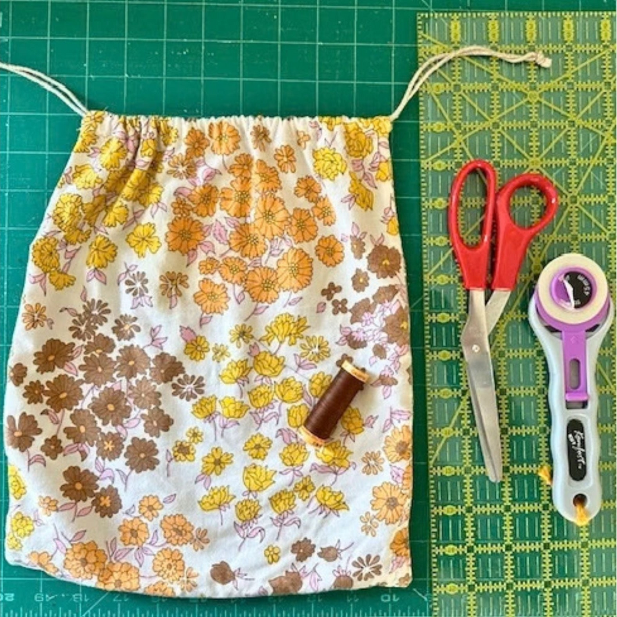 Beginner sewing workshop with Jasmine at Stitch & Knit Dartmouth — learn to sew a drawstring bag. A fabric drawstring bag, displayed alongside sewing tools including scissors, a rotary cutter, and a spool of thread on a green cutting mat.