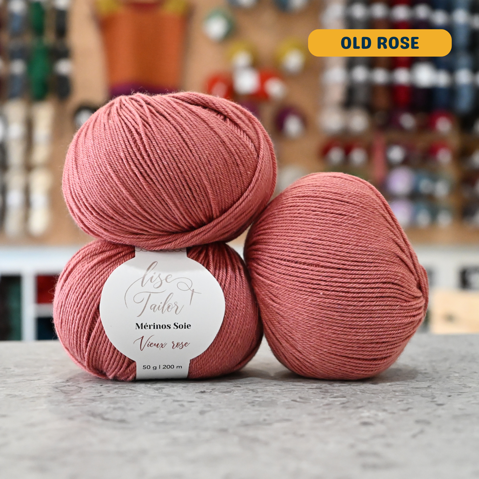 50g pink (old rose) merino & silk fingering yarn, 'Lise Tailor Merino Silk' label visible, craft shop background (blurred)