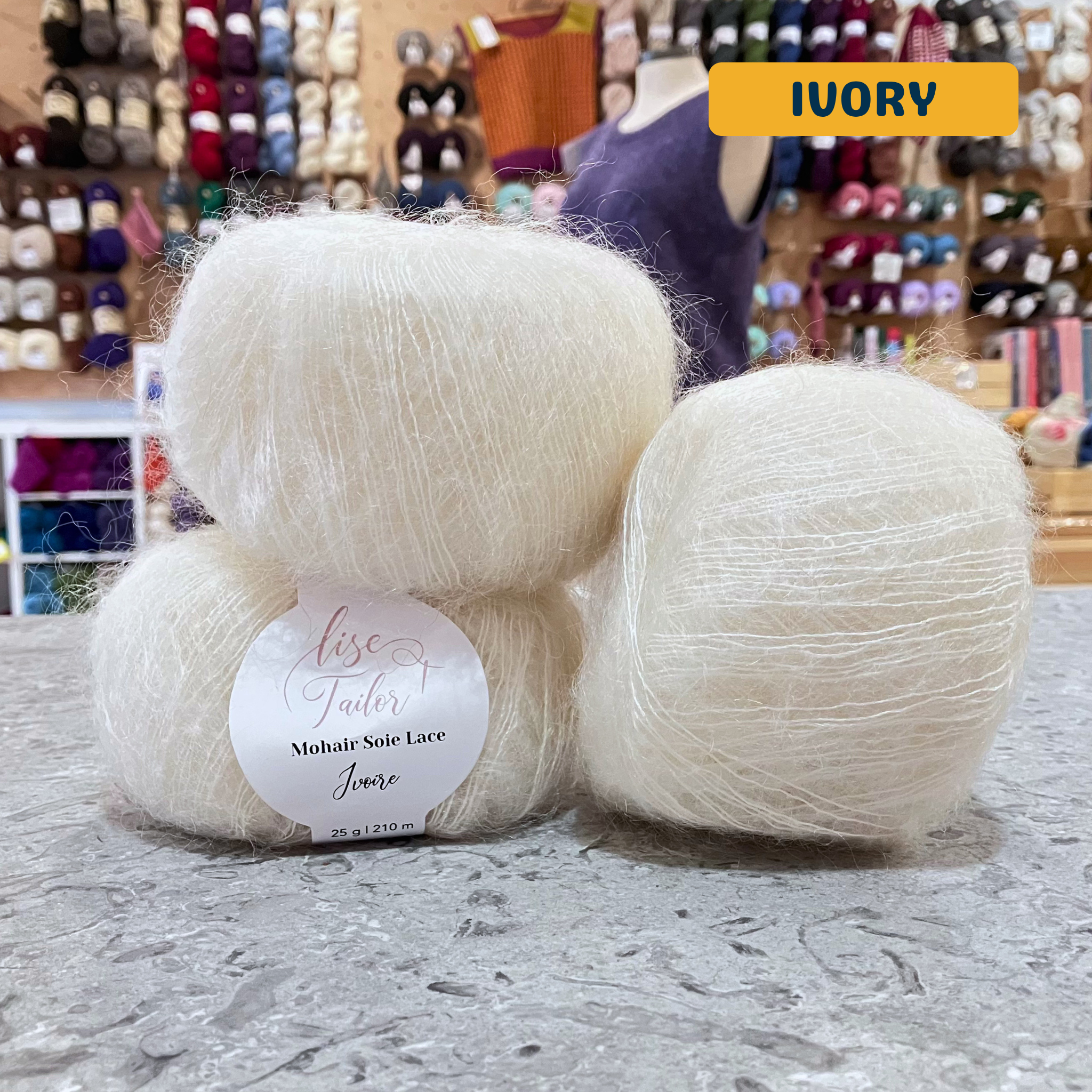 50g natural (ivory) mohair & silk lace yarn, 'Lise Tailor Mohair Silk Lace' label visible, craft shop background (blurred)