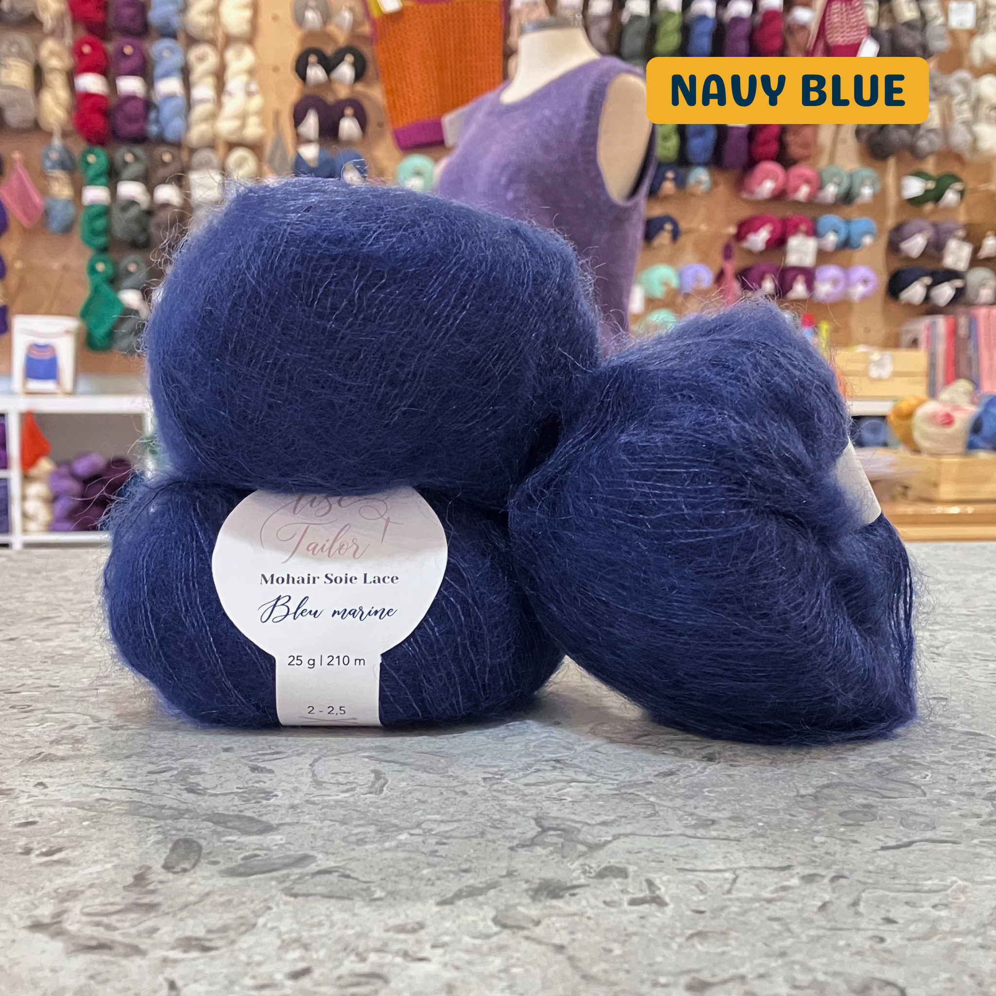 50g dark blue (navy) mohair & silk lace yarn, 'Lise Tailor Mohair Silk Lace' label visible, craft shop background (blurred)