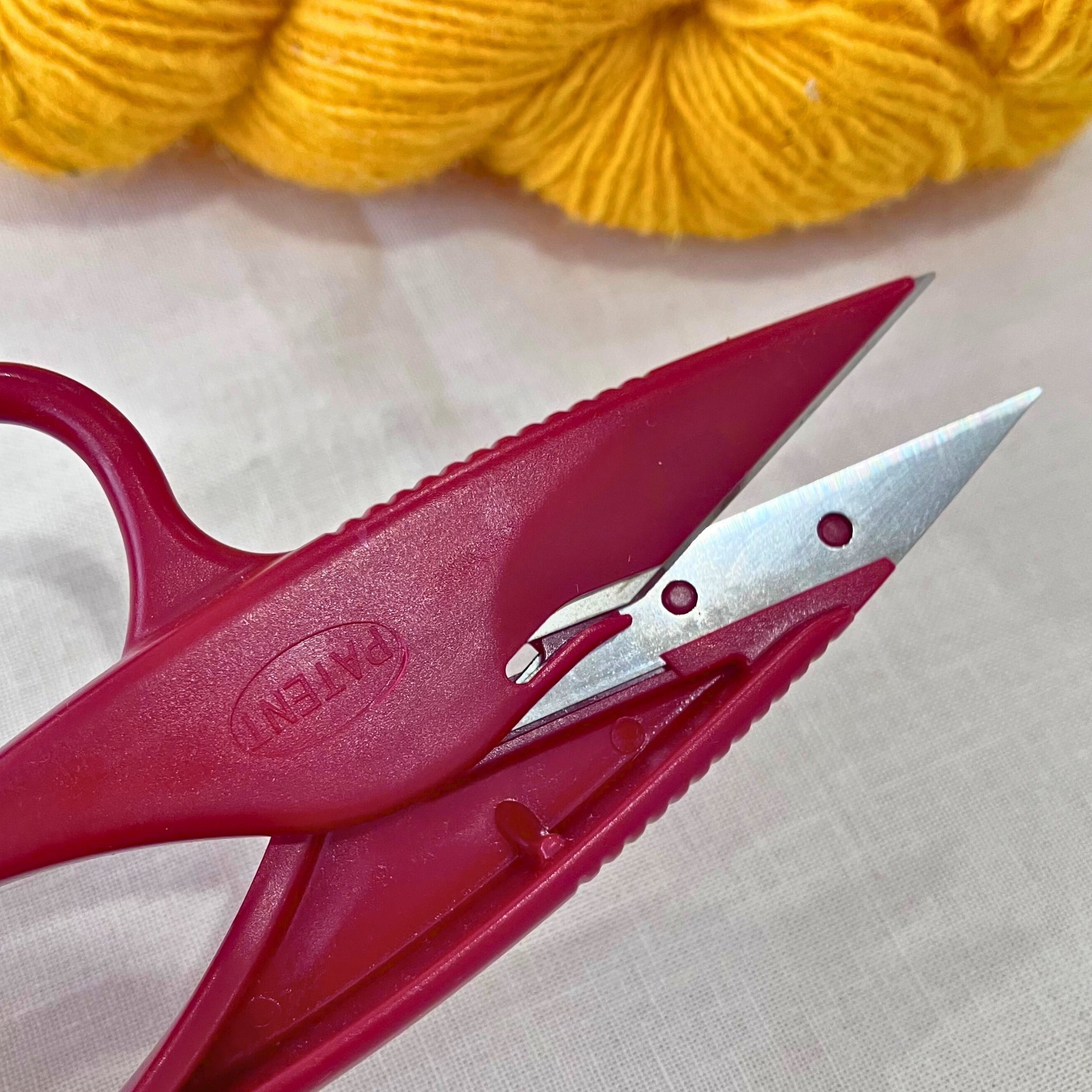 Close-up of Milward thread snips precision tip and stainless steel blades. Yellow yarn in background (blurred).