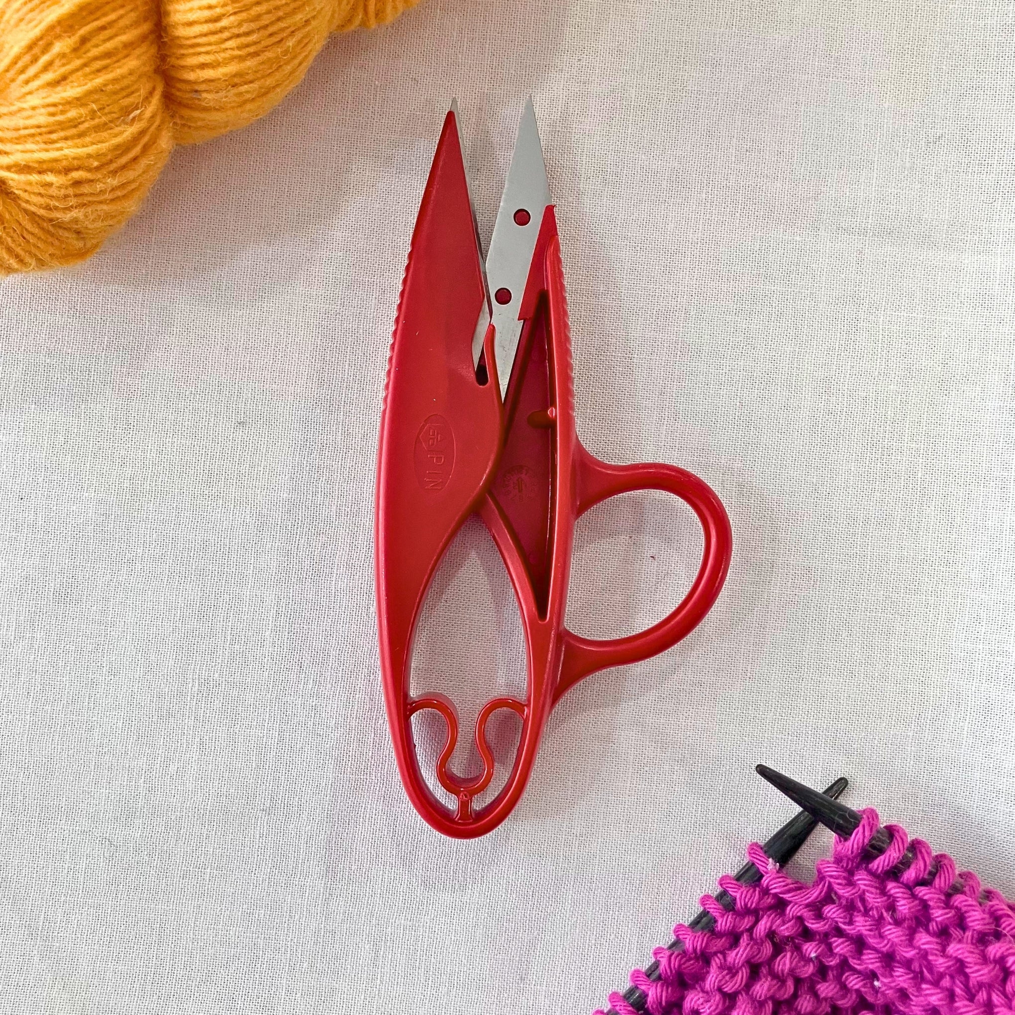 Red Milward 4.5 inch stainless steel thread snips on muslin fabric background.