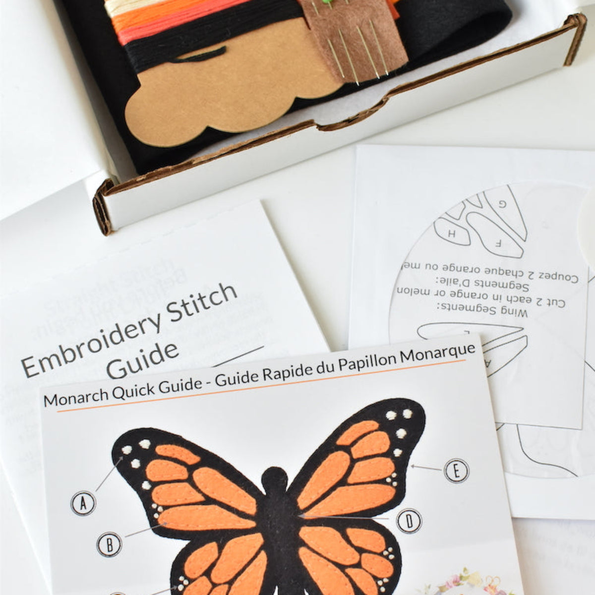 Embroidery stitch kit contents displayed in a box, including a butterfly embroidery guide, orange and black felt pieces, photographed on a white background.