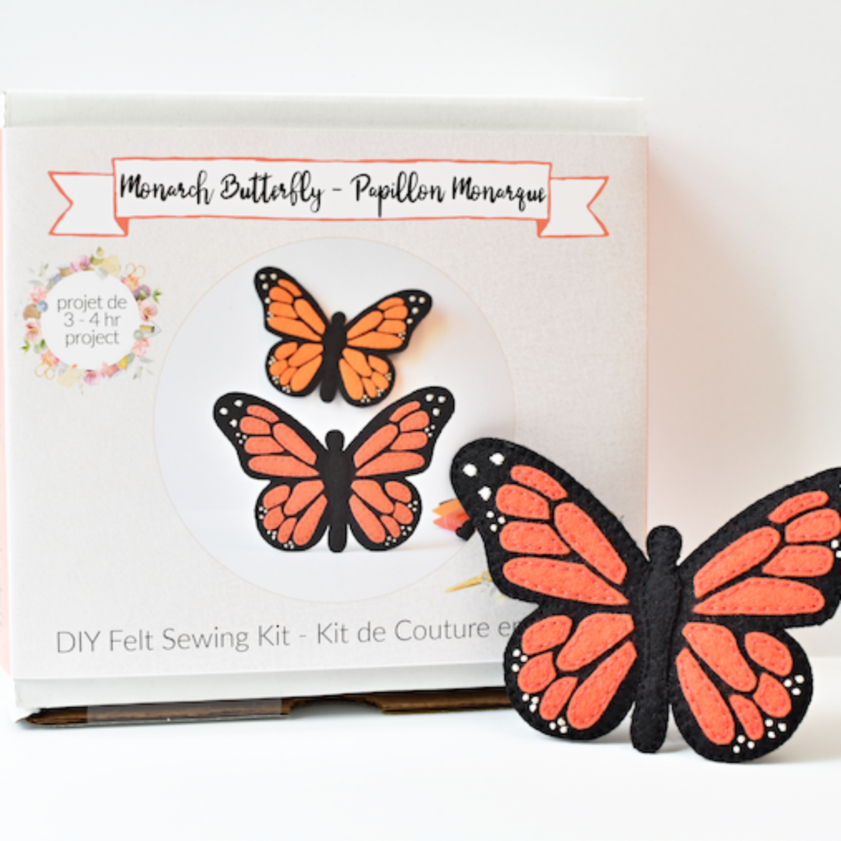A DIY felt sewing kit featuring monarch butterflies, with one finished orange and black felt butterfly placed in front of its white packaging box.