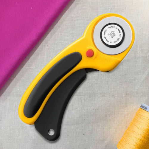 OLFA 45mm Deluxe Ergonomic Handle Rotary Cutter with anti-slip rubber grip and self-retracting safety blade. Purple fabric and yellow thread in background.